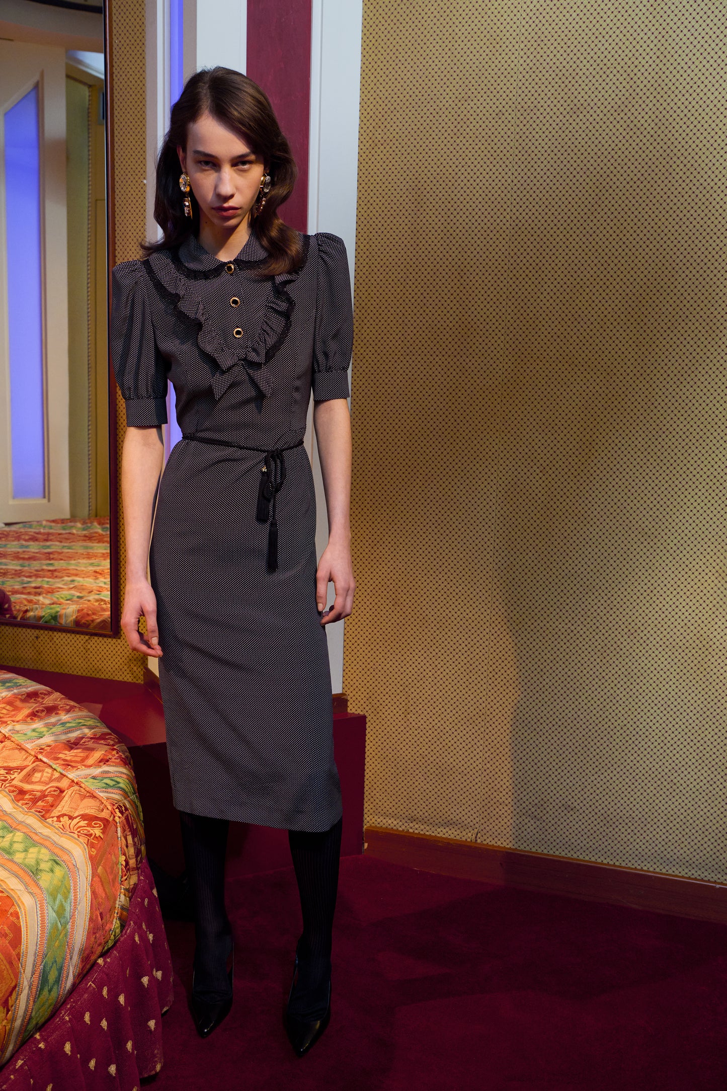 Black and white small polka-dot print silk crêpe de chine midi dress with short puffed sleeeves and black and old tone buttons. Finished with a lace trimmed collar and ruffled bib detailing.

Look 31 – Fall Winter 2026 Lookbook.