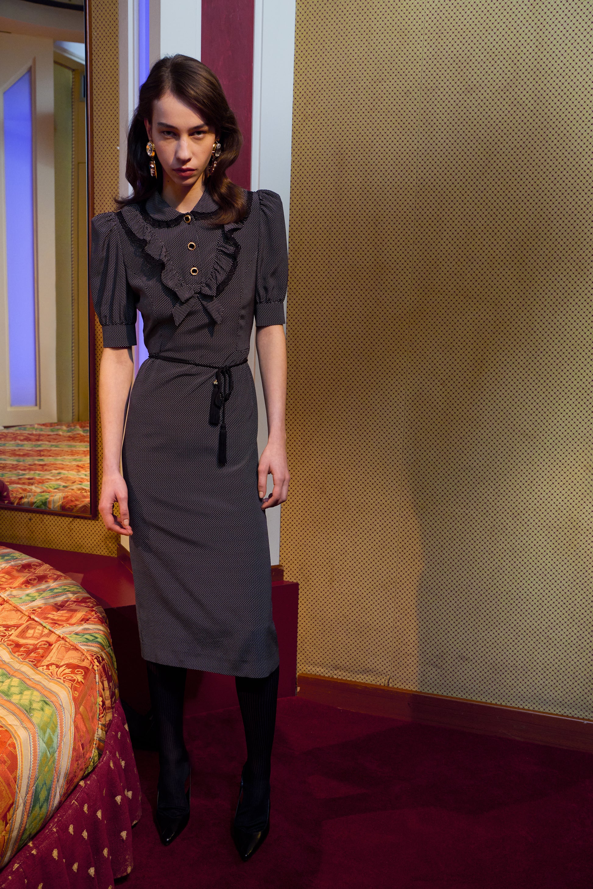 Black and white small polka-dot print silk crêpe de chine midi dress with short puffed sleeeves and black and old tone buttons. Finished with a lace trimmed collar and ruffled bib detailing.

Look 31 – Fall Winter 2026 Lookbook.