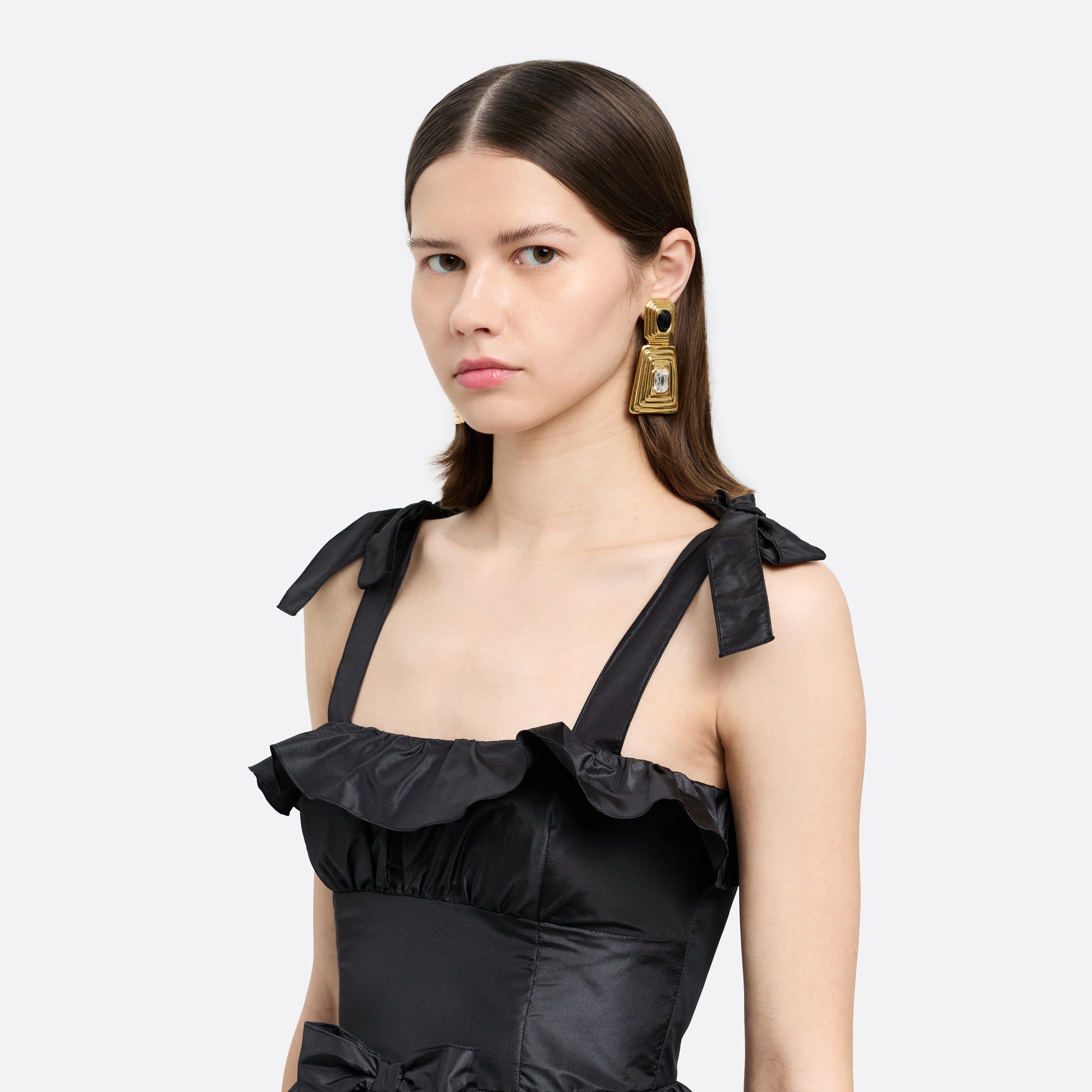 Gold-tone metal clip-on earrings with a black crystal detail and clear crystal pendant drop.

Featured in the Fall Winter 2026 Lookbook.