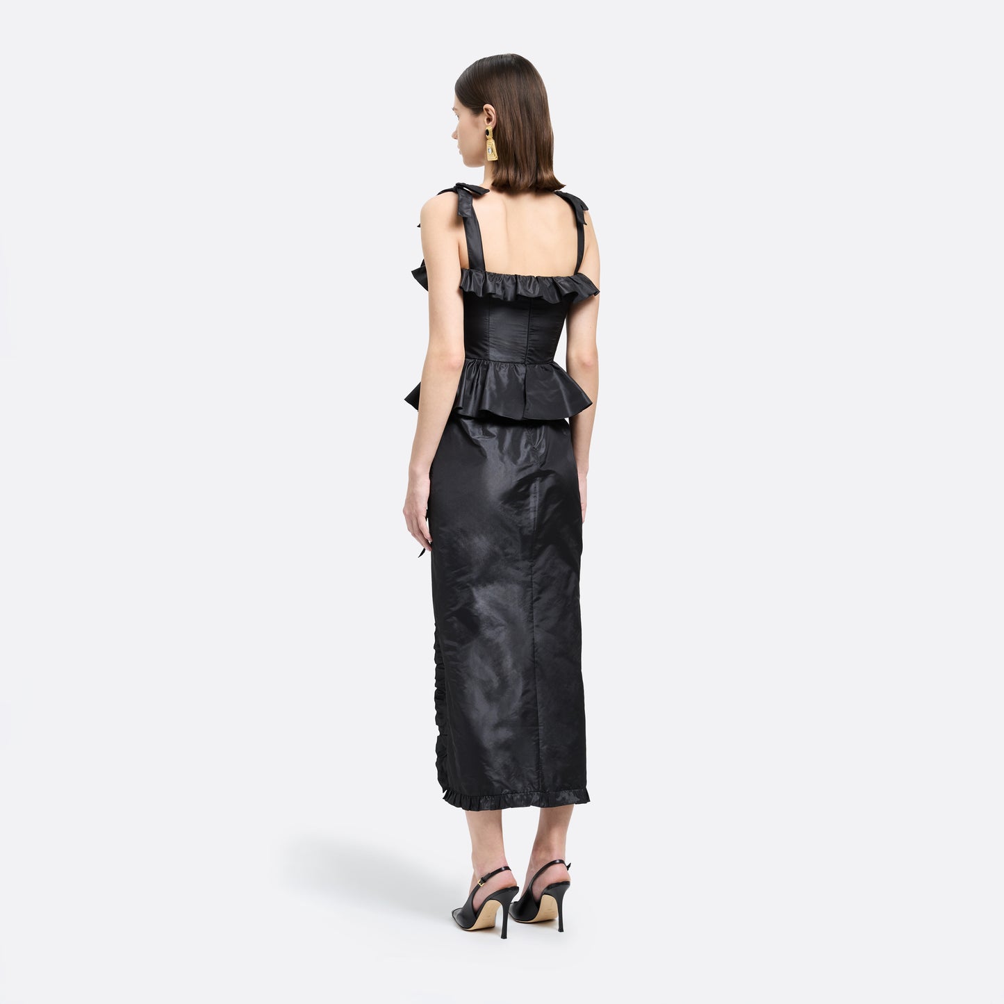Black silk taffeta midi dress with self-tie shoulder straps and a ruffled neckline. A peplum defines the silhouette, while the straight skirt is finished with a delicate ruffle trim at the split.

Look 22 – Fall Winter 2026 Lookbook.