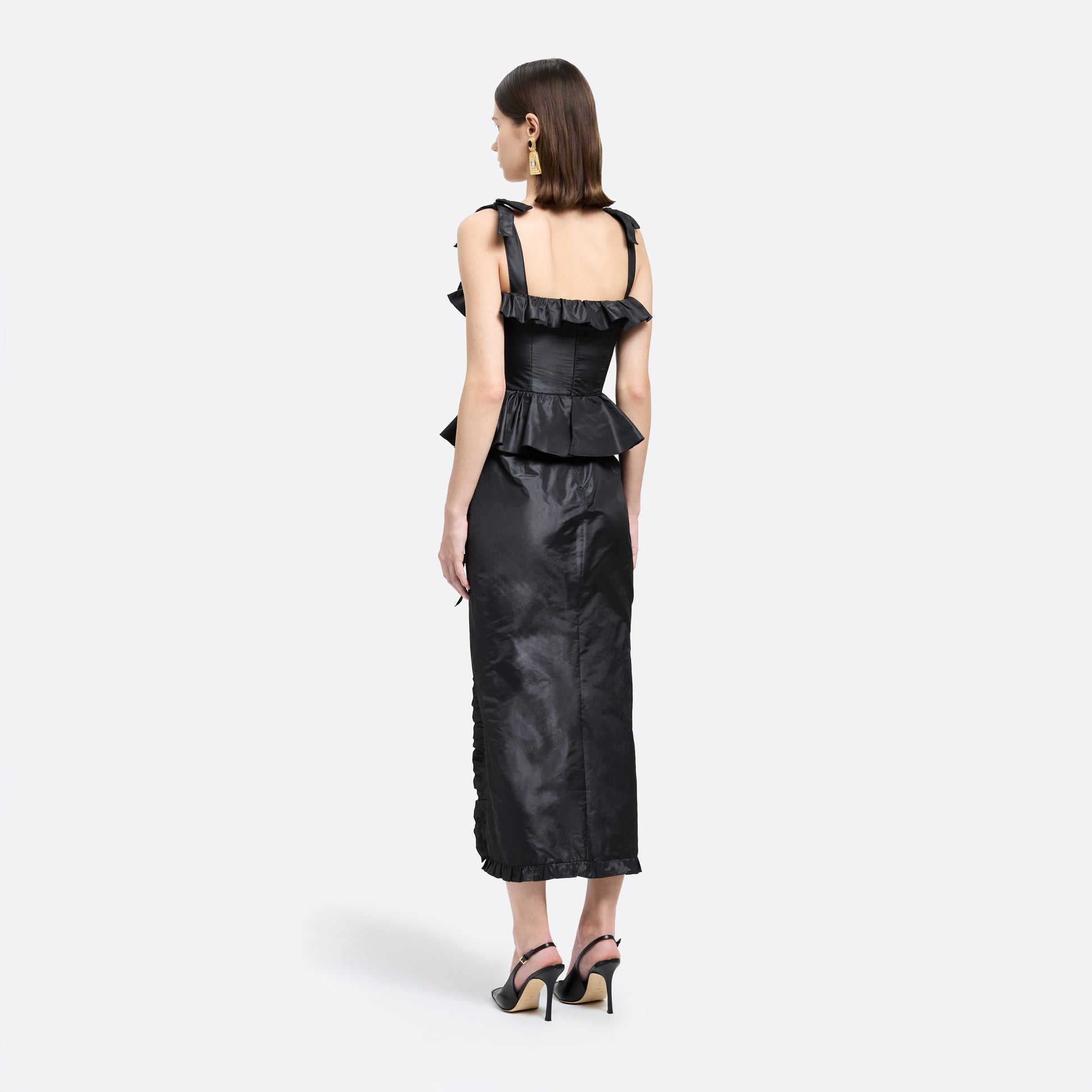 Black silk taffeta midi dress with self-tie shoulder straps and a ruffled neckline. A peplum defines the silhouette, while the straight skirt is finished with a delicate ruffle trim at the split.

Look 22 – Fall Winter 2026 Lookbook.