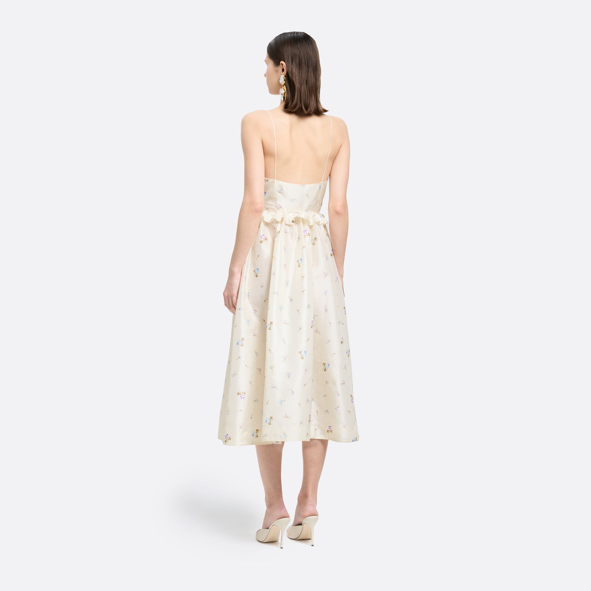 Floral-print white silk taffeta midi dress with spaghetti straps and a scoop neckline. The silhouette is finished with a flared skirt with pockets and a ruffled waist with a bow.