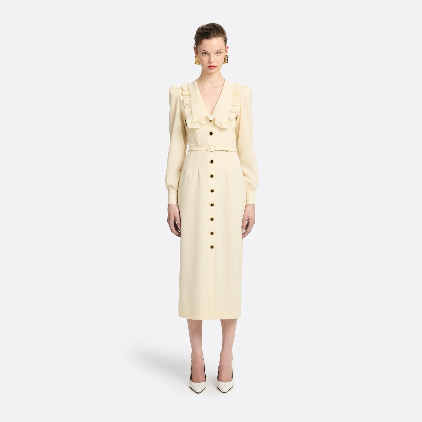 Cream light wool crêpe midi dress with a deep V-neckline framed by a ruffle-trimmed collar and long sleeves. Finished with a front button closure accented by black and gold-tone buttons and a slim belt.

Look 10 – Fall Winter 2026 Lookbook.