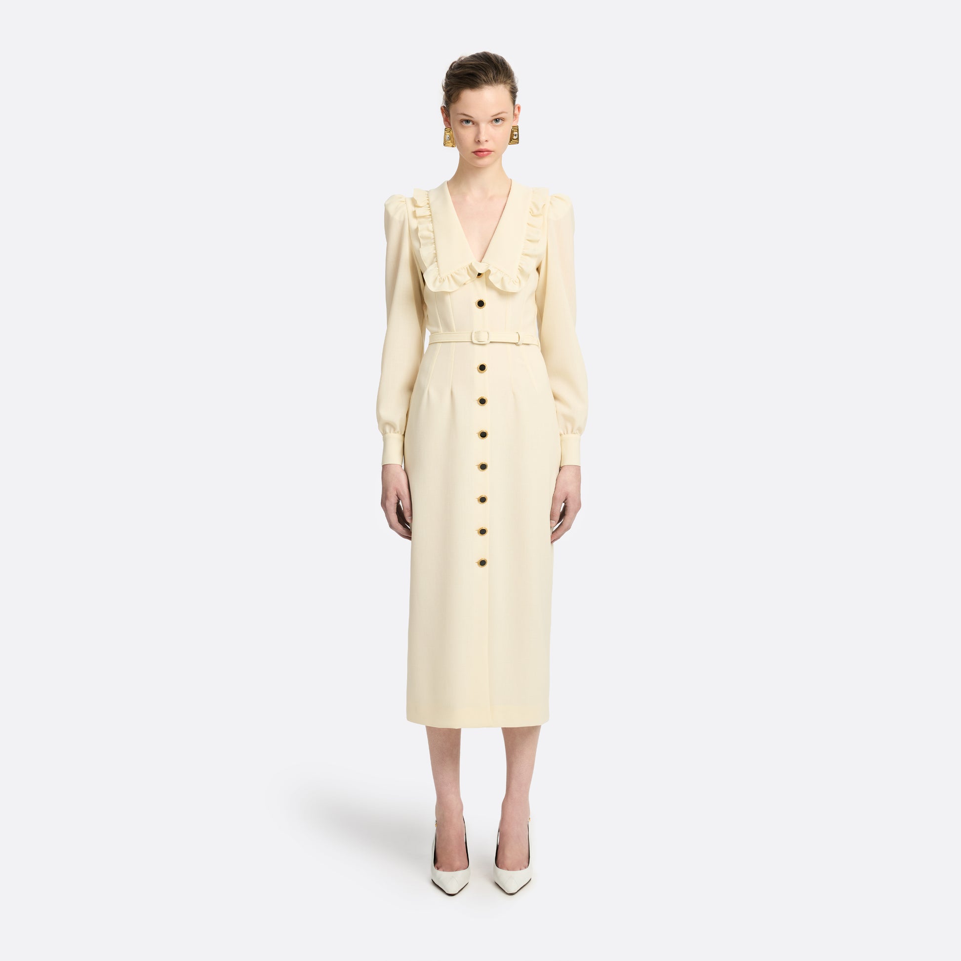Cream light wool crêpe midi dress with a deep V-neckline framed by a ruffle-trimmed collar and long sleeves. Finished with a front button closure accented by black and gold-tone buttons and a slim belt.

Look 10 – Fall Winter 2026 Lookbook.