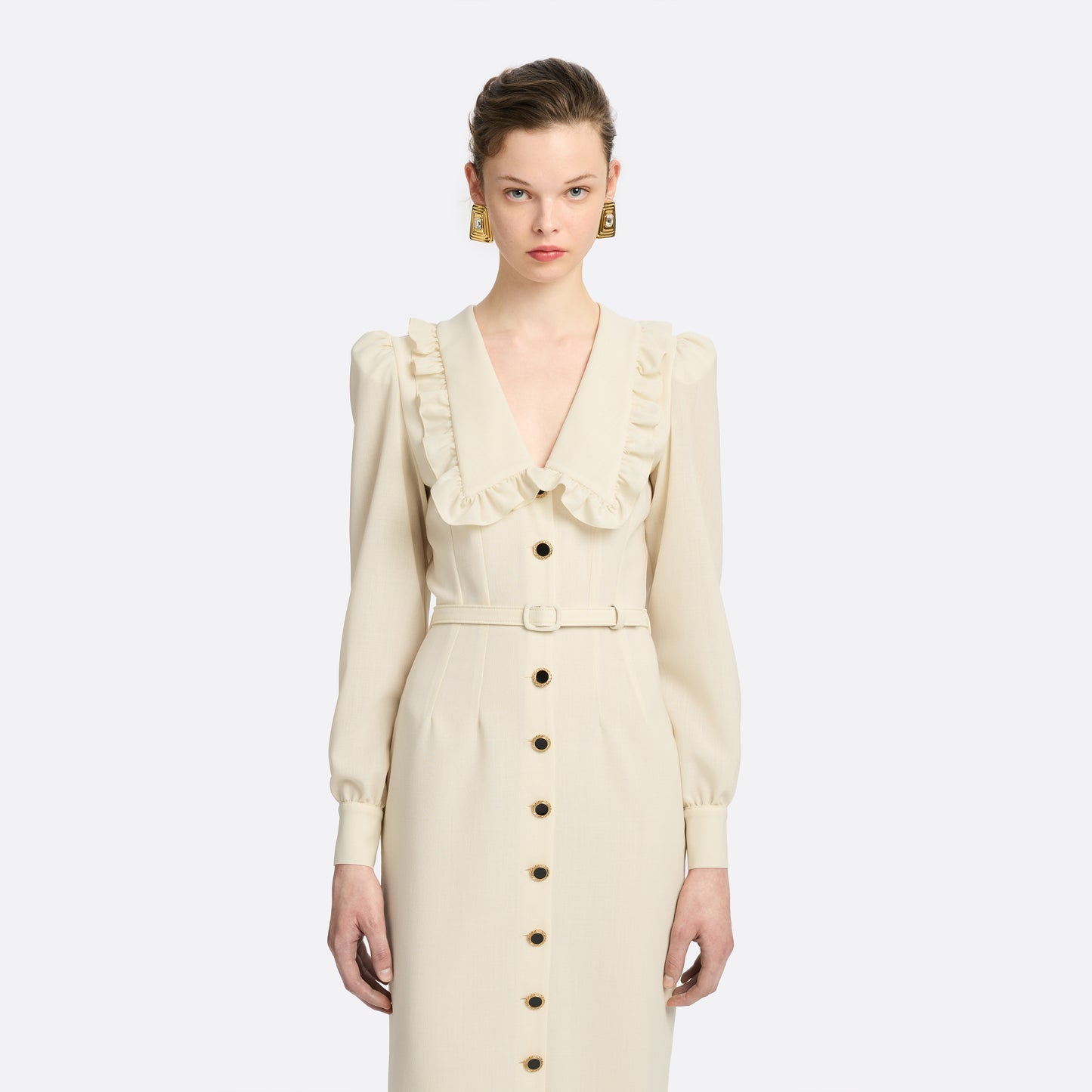 Cream light wool crêpe midi dress with a deep V-neckline framed by a ruffle-trimmed collar and long sleeves. Finished with a front button closure accented by black and gold-tone buttons and a slim belt.

Look 10 – Fall Winter 2026 Lookbook.