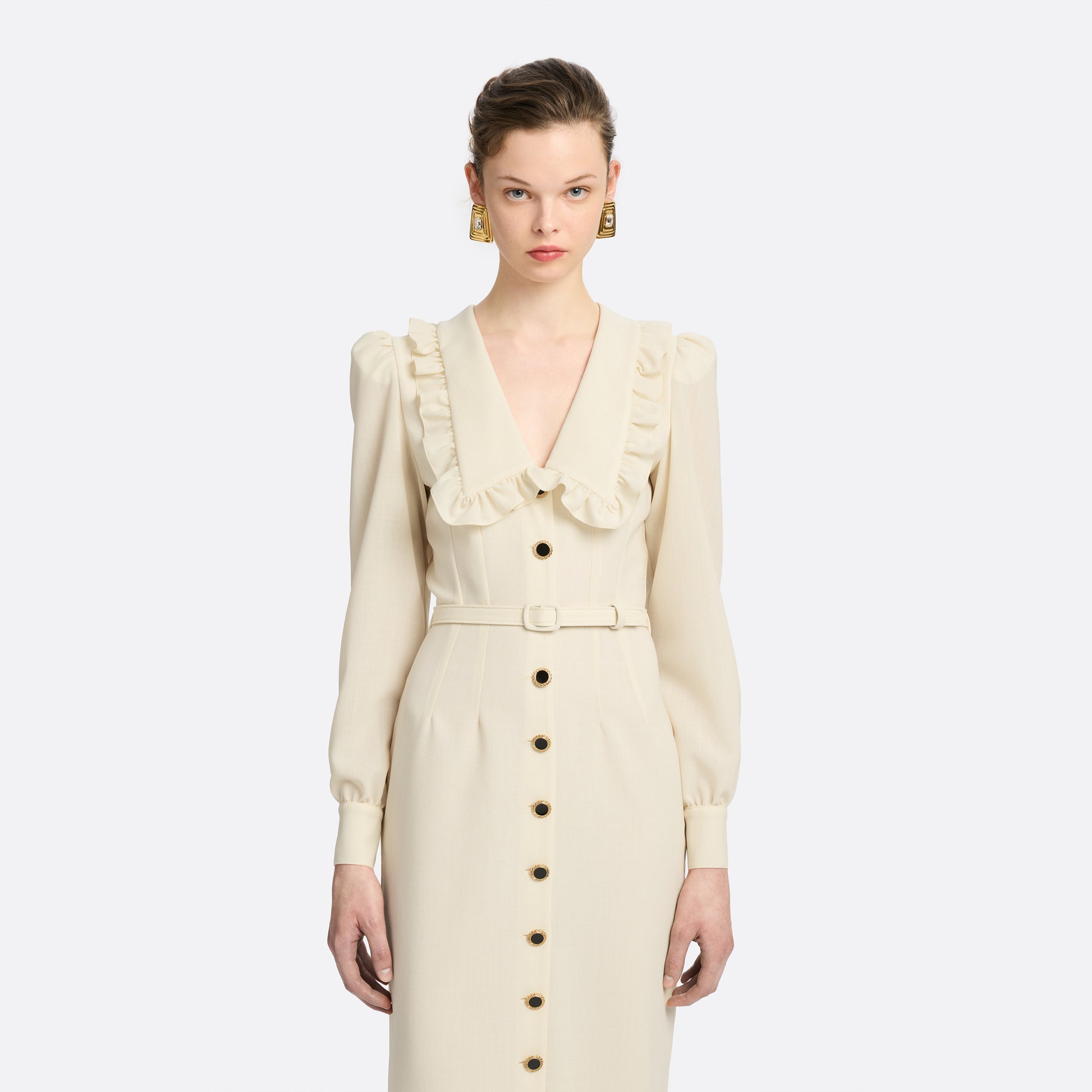 Cream light wool crêpe midi dress with a deep V-neckline framed by a ruffle-trimmed collar and long sleeves. Finished with a front button closure accented by black and gold-tone buttons and a slim belt.

Look 10 – Fall Winter 2026 Lookbook.