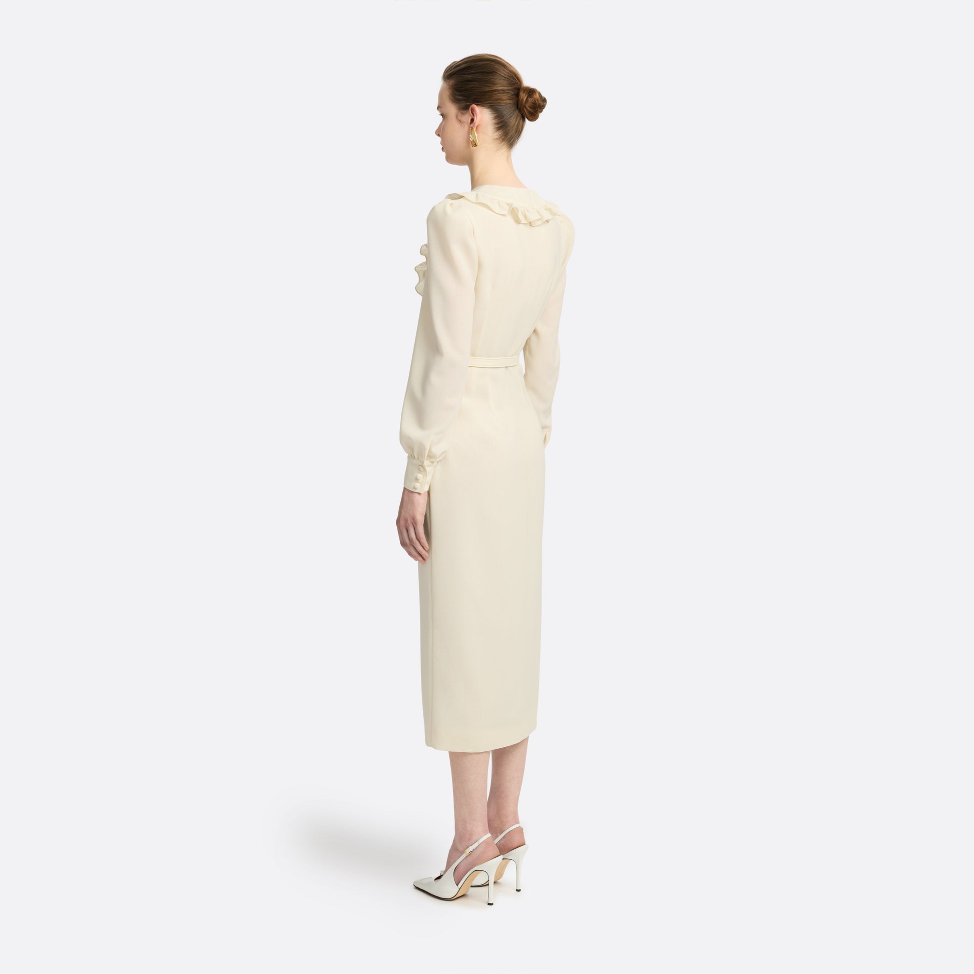 Cream light wool crêpe midi dress with a deep V-neckline framed by a ruffle-trimmed collar and long sleeves. Finished with a front button closure accented by black and gold-tone buttons and a slim belt.

Look 10 – Fall Winter 2026 Lookbook.