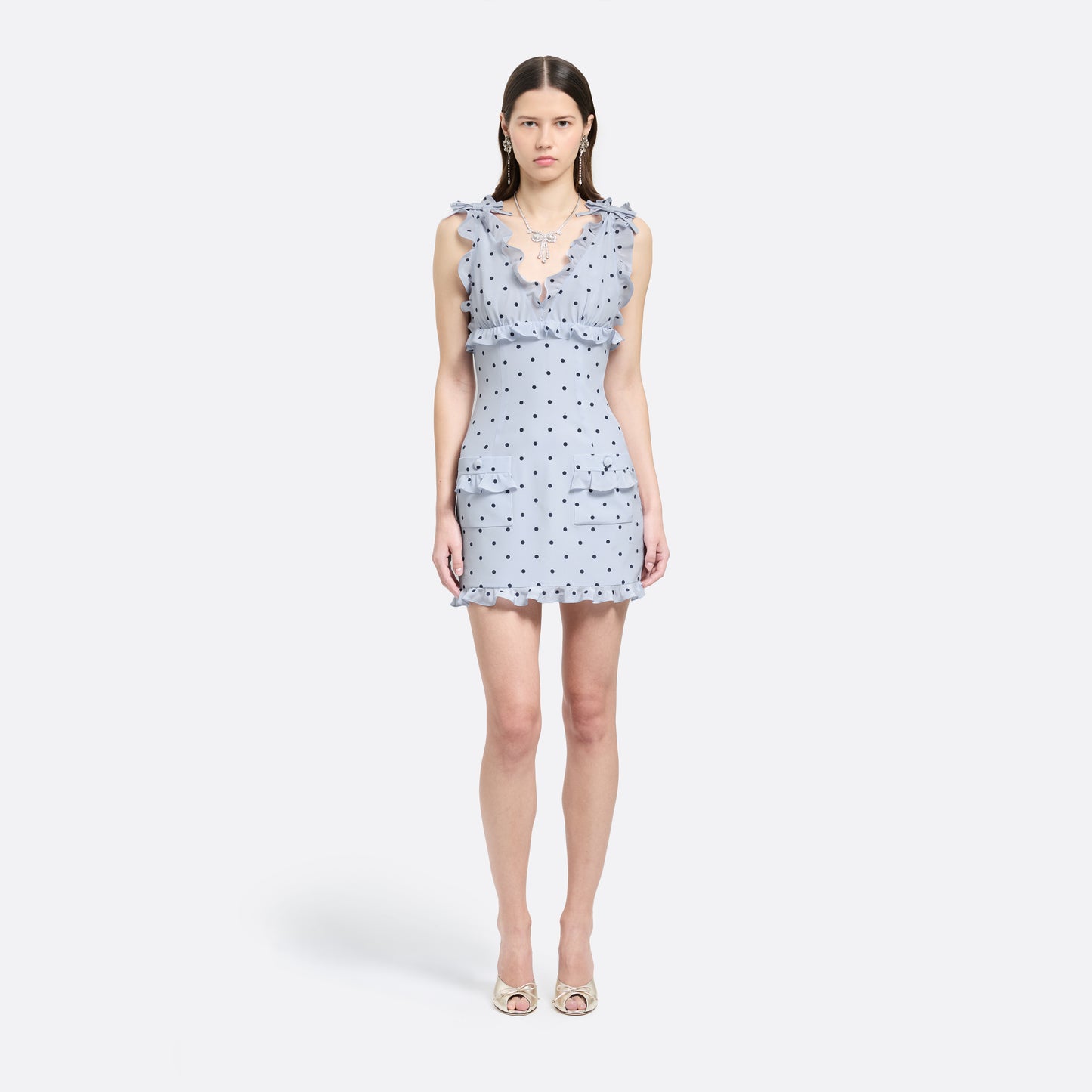 Light blue polka-dot silk crêpe de chine mini dress with bow-detailed shoulder straps and a ruffled neckline. The fitted silhouette is finished with patch pockets and a ruffled hem.