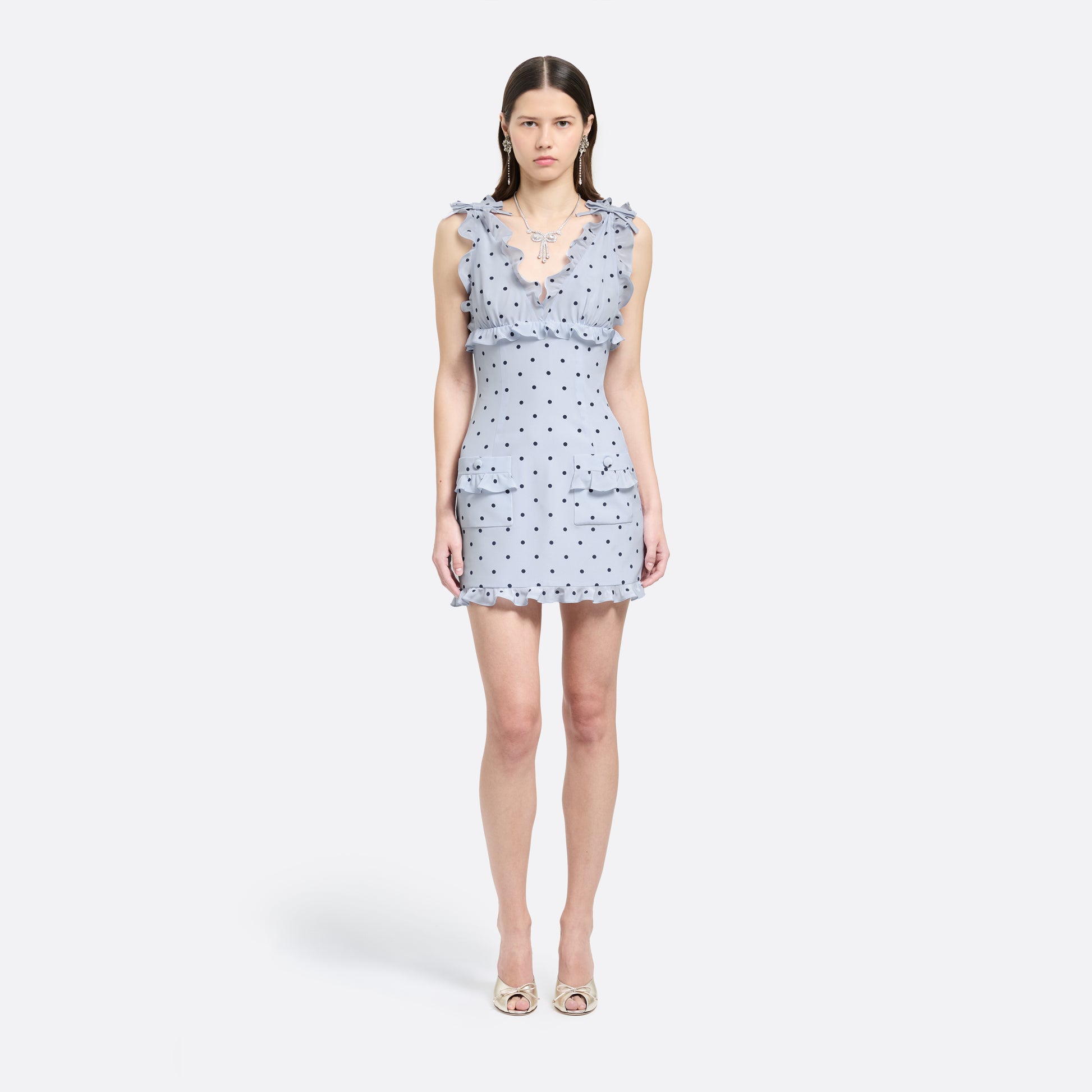 Light blue polka-dot silk crêpe de chine mini dress with bow-detailed shoulder straps and a ruffled neckline. The fitted silhouette is finished with patch pockets and a ruffled hem.