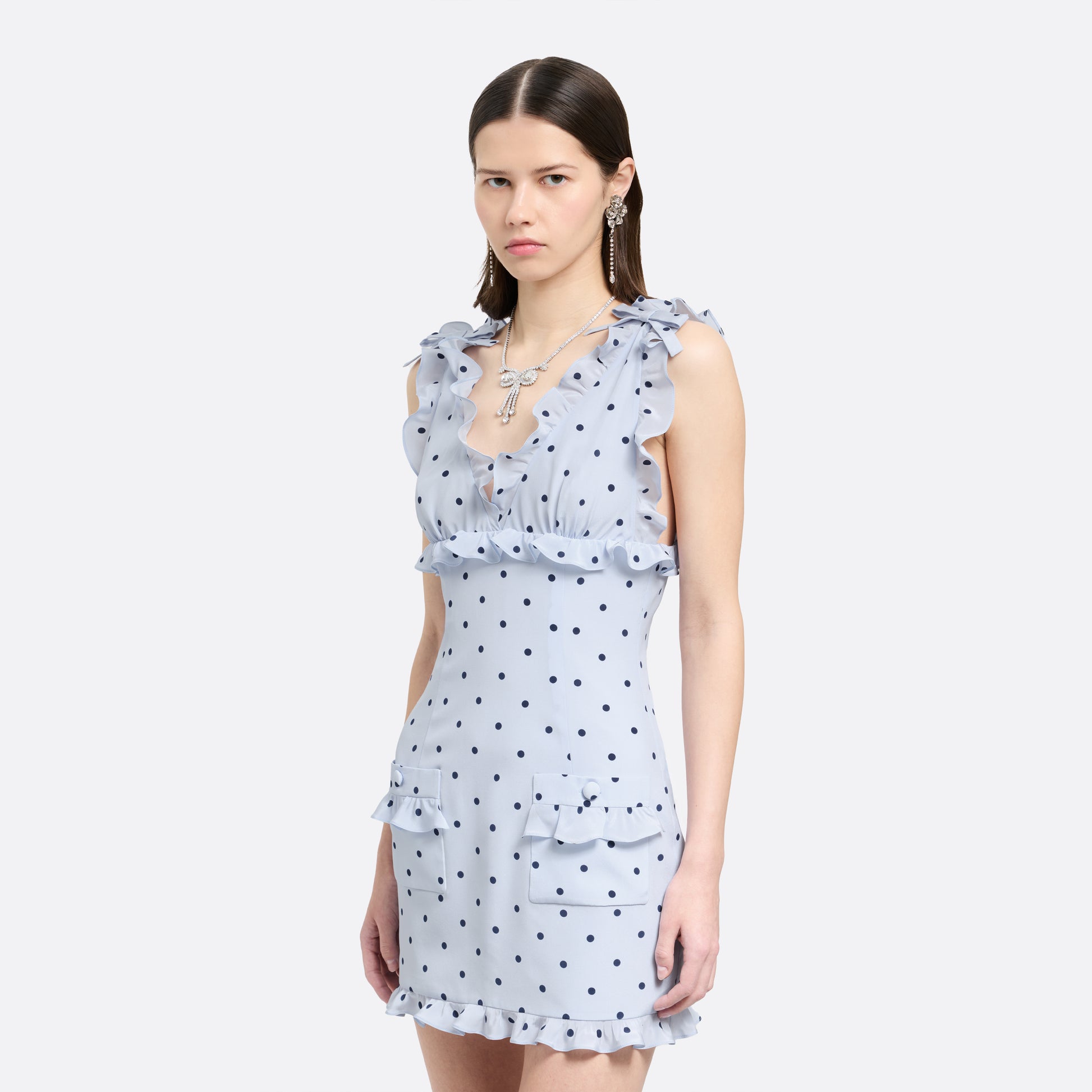 Light blue polka-dot silk crêpe de chine mini dress with bow-detailed shoulder straps and a ruffled neckline. The fitted silhouette is finished with patch pockets and a ruffled hem.