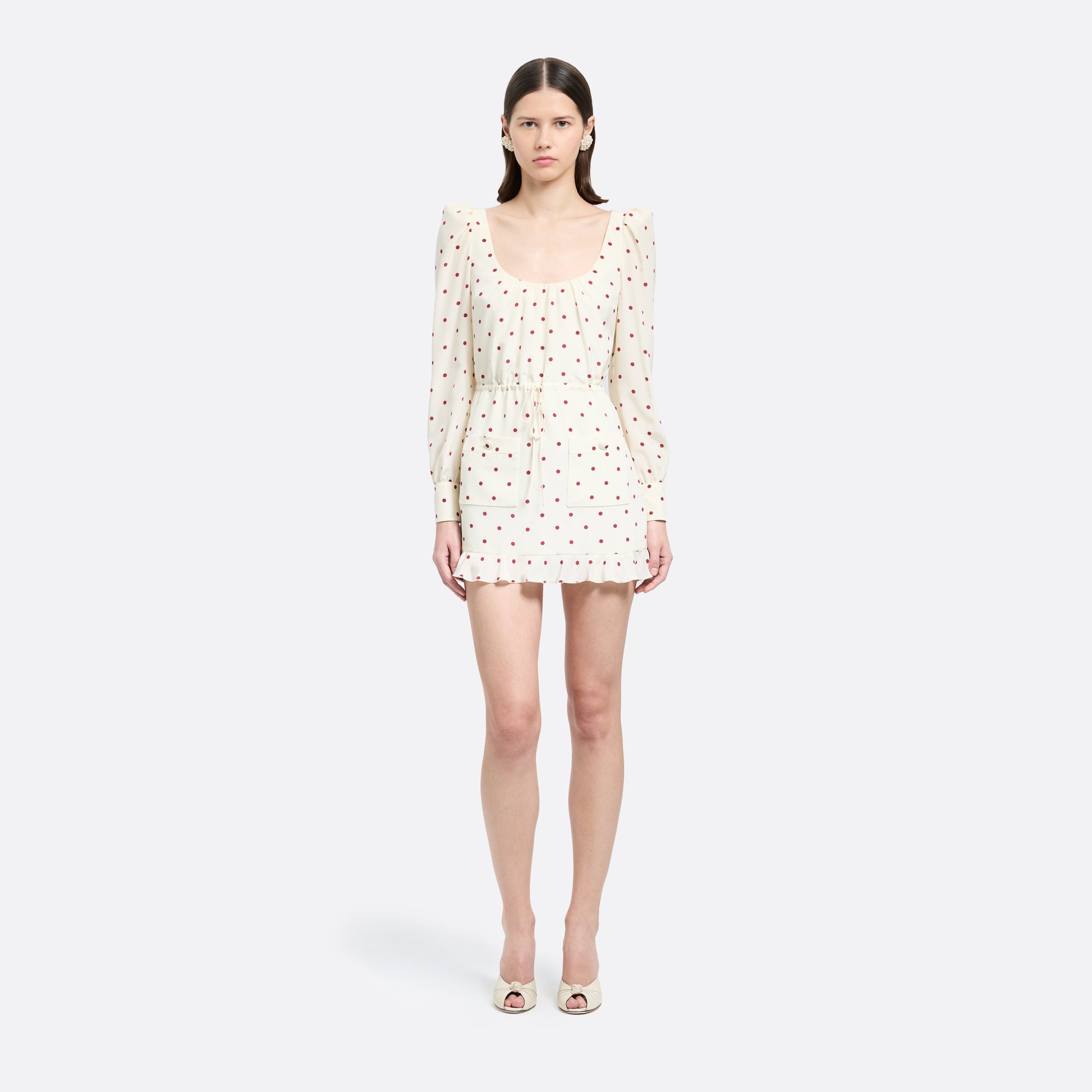 Cream and bordeaux polka-dot silk crêpe de chine mini dress with a scooped neckline and long sleeves. Defined by a drawstring waist, the silhouette is finished with patch pockets and a volant hem.