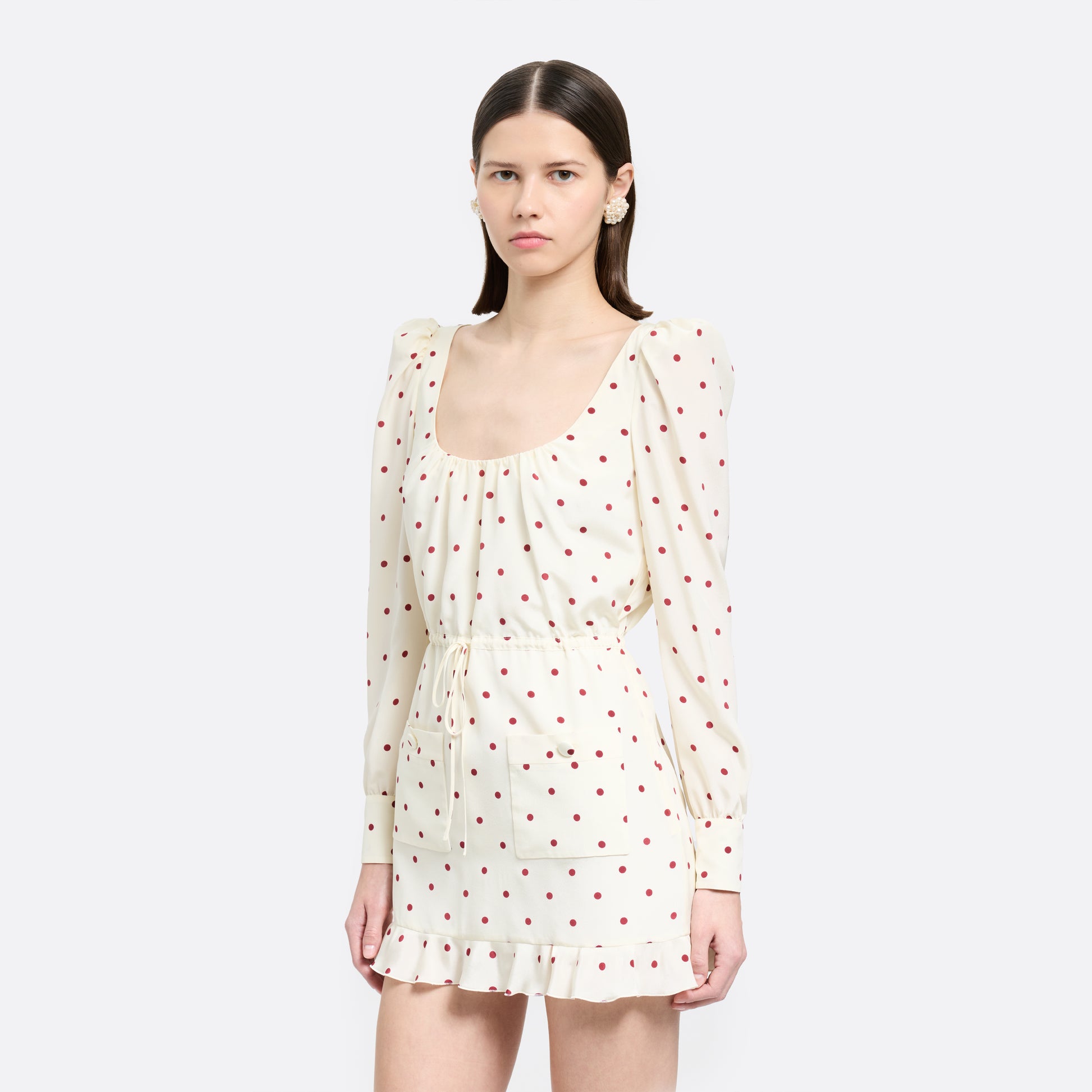Cream and bordeaux polka-dot silk crêpe de chine mini dress with a scooped neckline and long sleeves. Defined by a drawstring waist, the silhouette is finished with patch pockets and a volant hem.