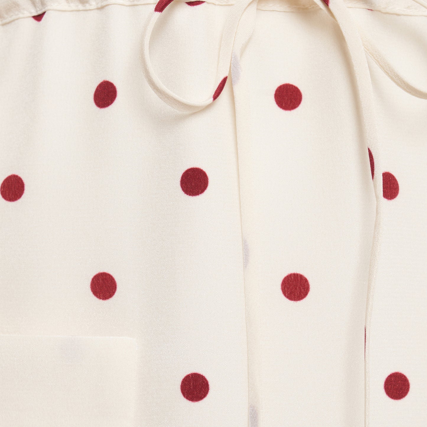 Cream and bordeaux polka-dot silk crêpe de chine mini dress with a scooped neckline and long sleeves. Defined by a drawstring waist, the silhouette is finished with patch pockets and a volant hem.