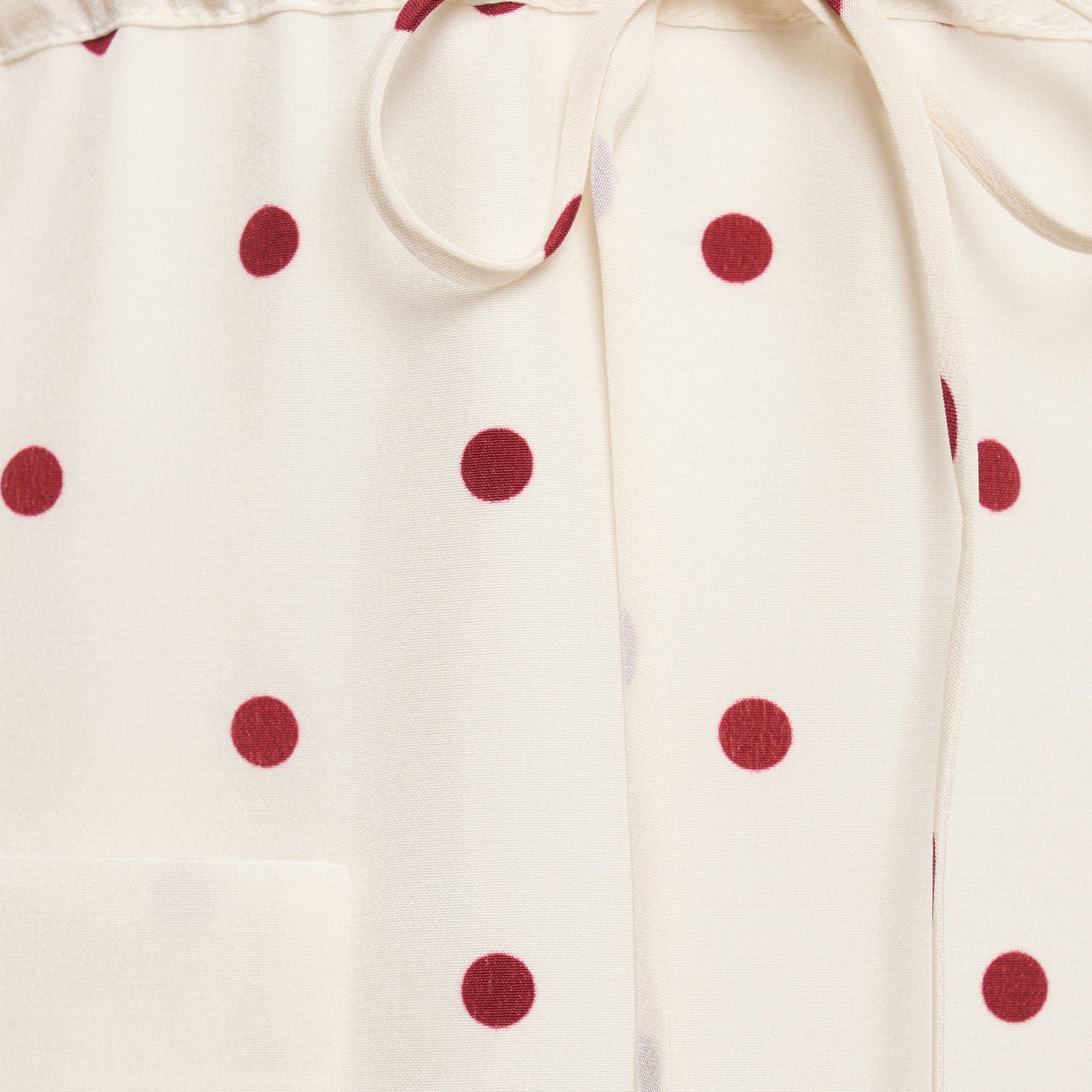 Cream and bordeaux polka-dot silk crêpe de chine mini dress with a scooped neckline and long sleeves. Defined by a drawstring waist, the silhouette is finished with patch pockets and a volant hem.