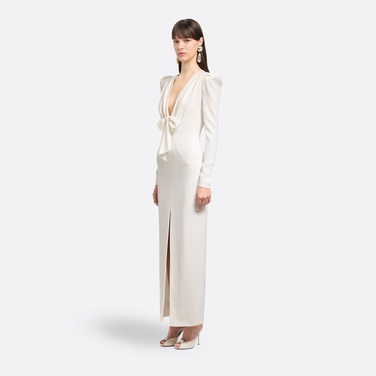 White cady evening dress cut to a fitted silhouette with a V-neckline and long sleeves. Finished with a bow detail and front split.