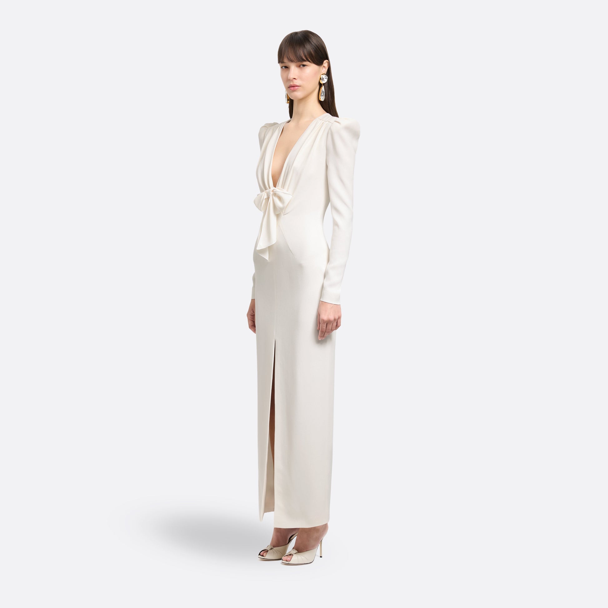 White cady evening dress cut to a fitted silhouette with a V-neckline and long sleeves. Finished with a bow detail and front split.