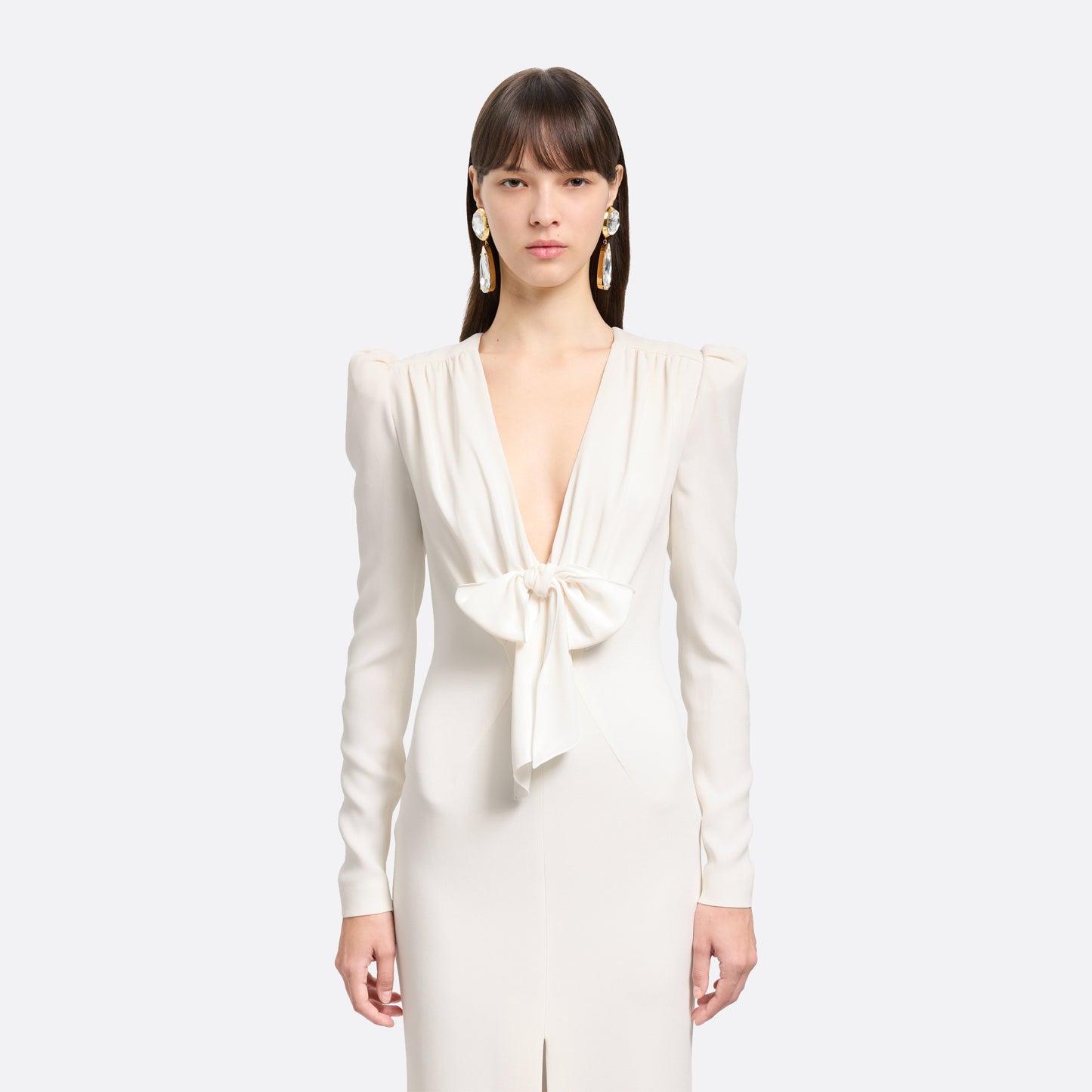 White cady evening dress cut to a fitted silhouette with a V-neckline and long sleeves. Finished with a bow detail and front split.
