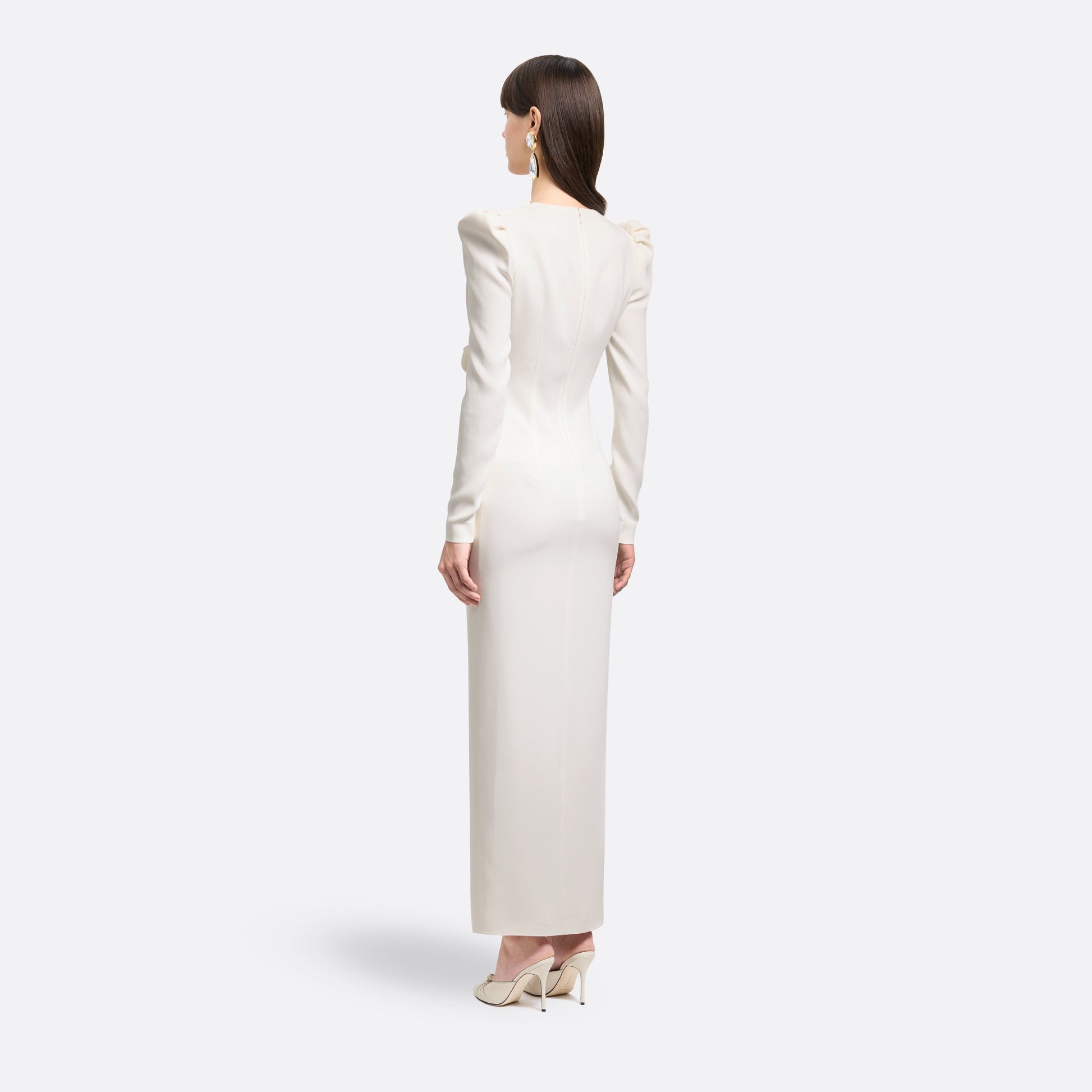 White cady evening dress cut to a fitted silhouette with a V-neckline and long sleeves. Finished with a bow detail and front split.