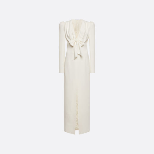 White cady evening dress cut to a fitted silhouette with a V-neckline and long sleeves. Finished with a bow detail and front split.