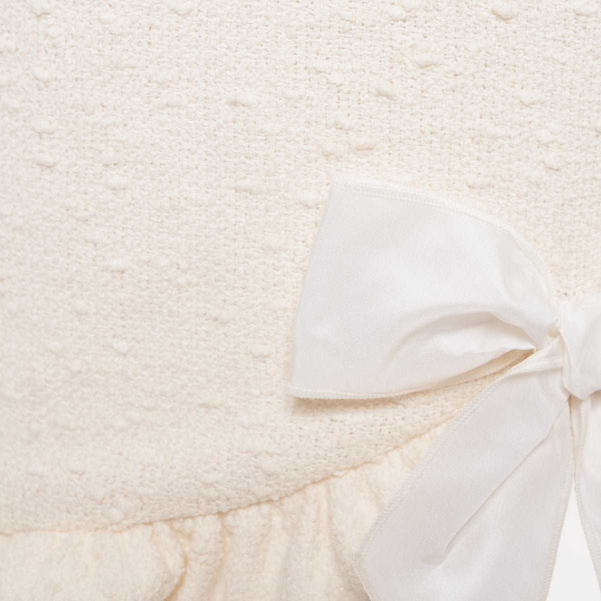 White tweed bouclé mini dress with a fitted silhouette and a soft ruffle at the hem. The shoulder straps are finished with silk bows.