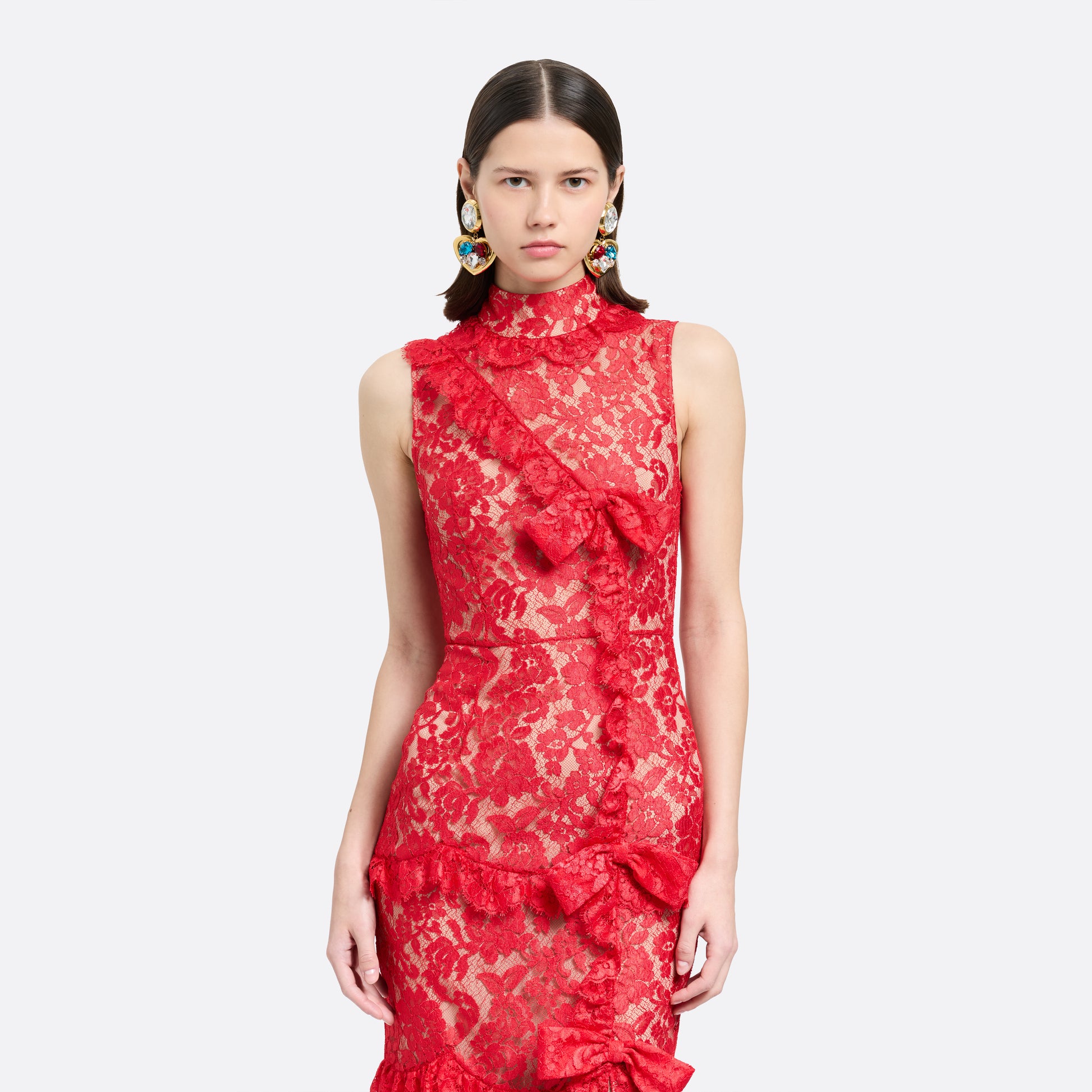 Red lace sleeveless evening dress with a high neckline and a fitted silhouette with a split. Finished with ruffled trims and bows.