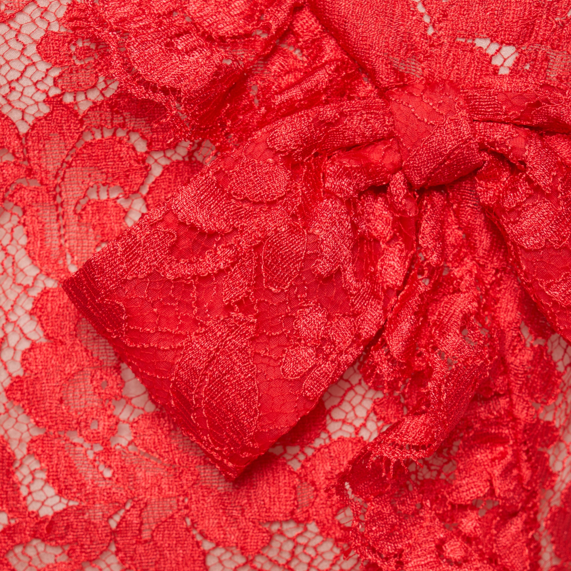 Red lace sleeveless evening dress with a high neckline and a fitted silhouette with a split. Finished with ruffled trims and bows.