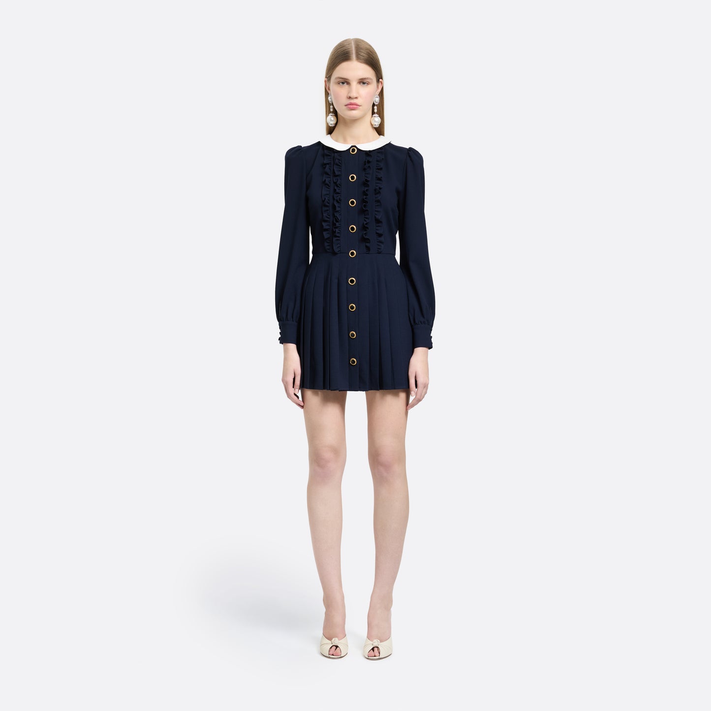 Navy blue light wool crêpe mini dress with a front button closure with black and gold tone buttons and a pleated skirt. Finished with a contrast collar and ruffle details.