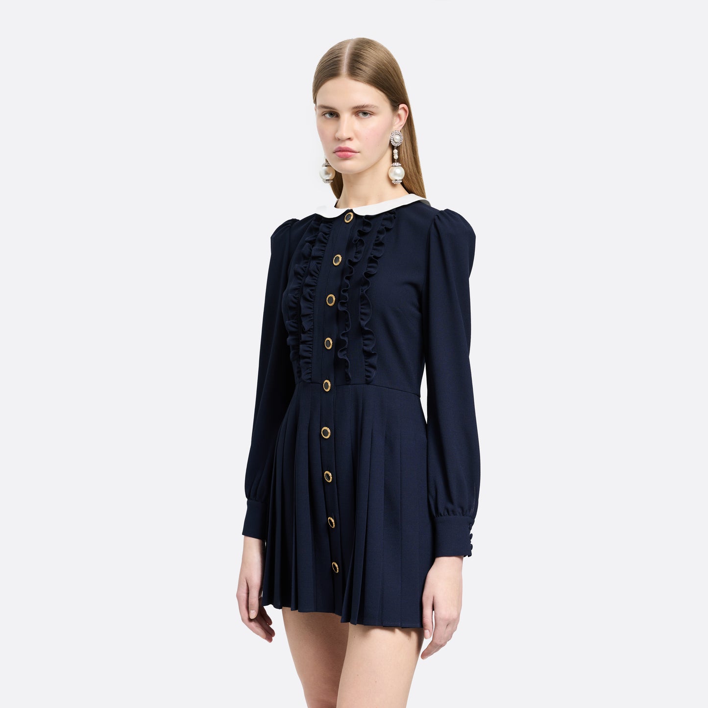 Navy blue light wool crêpe mini dress with a front button closure with black and gold tone buttons and a pleated skirt. Finished with a contrast collar and ruffle details.