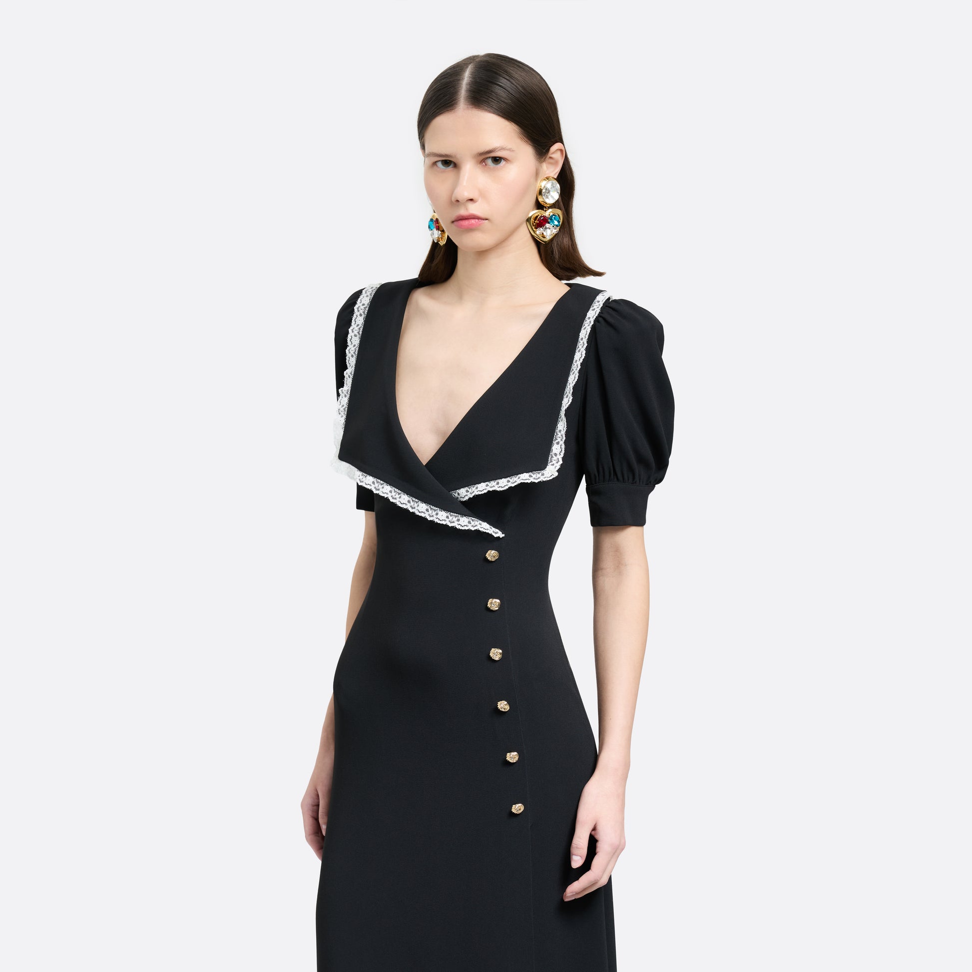 Black cady midi dress with a wrap-style silhouette and asymmetric button detailing. The wide collar is finished with a white lace trim.

Look 23 – Fall Winter 2026 Lookbook.