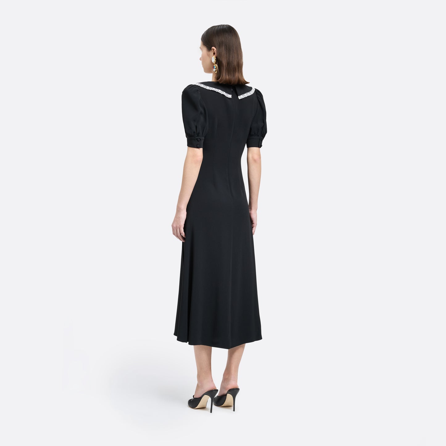 Black cady midi dress with a wrap-style silhouette and asymmetric button detailing. The wide collar is finished with a white lace trim.

Look 23 – Fall Winter 2026 Lookbook.