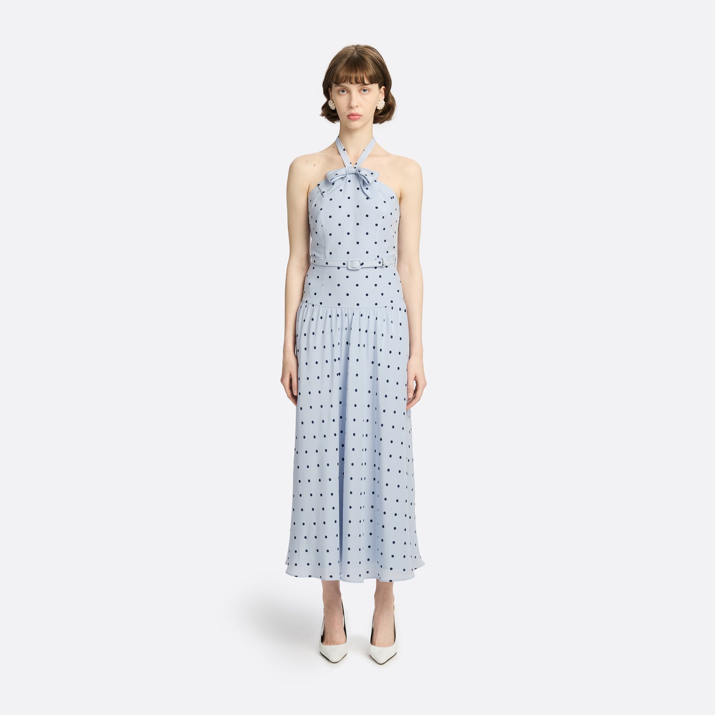 Light blue polka-dot silk crêpe de chine halterneck dress with a bow detail at the neckline. Defined by a fitted waist with a slim belt, the silhouette is finished with a flared skirt.