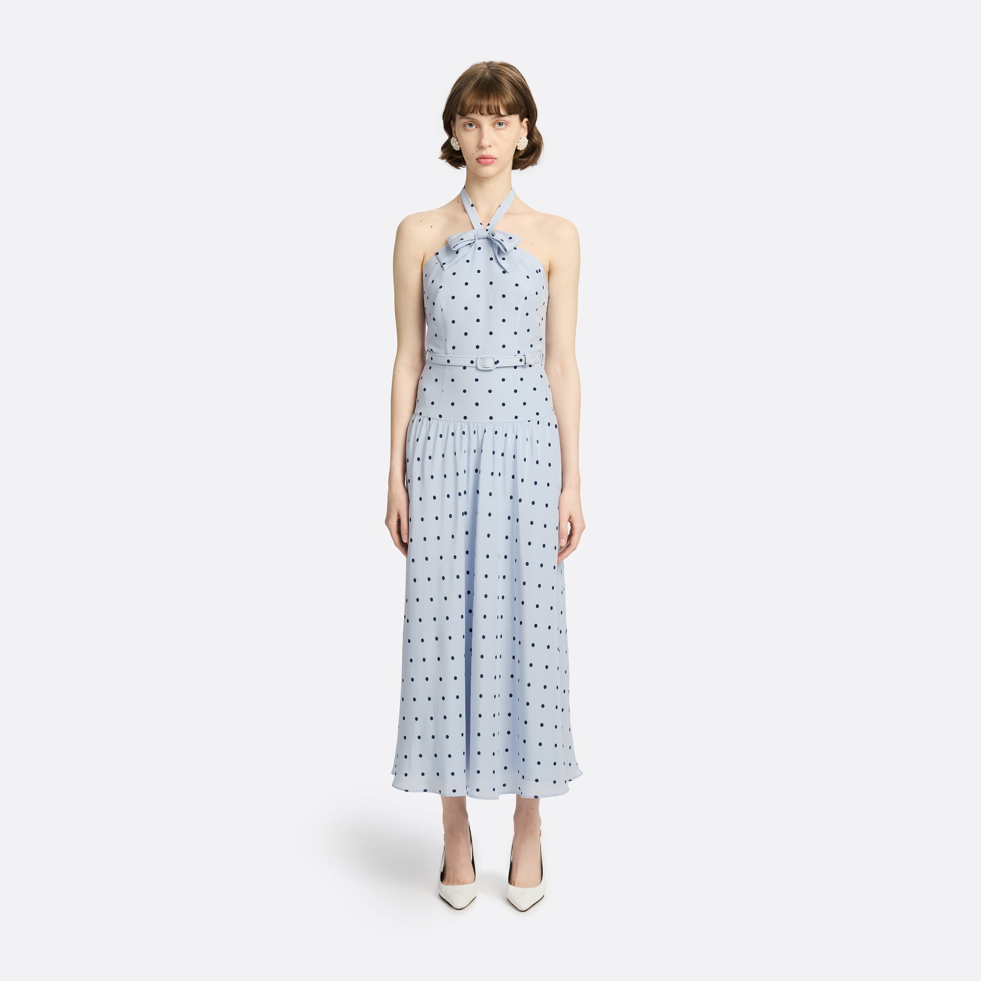 Light blue polka-dot silk crêpe de chine halterneck dress with a bow detail at the neckline. Defined by a fitted waist with a slim belt, the silhouette is finished with a flared skirt.
