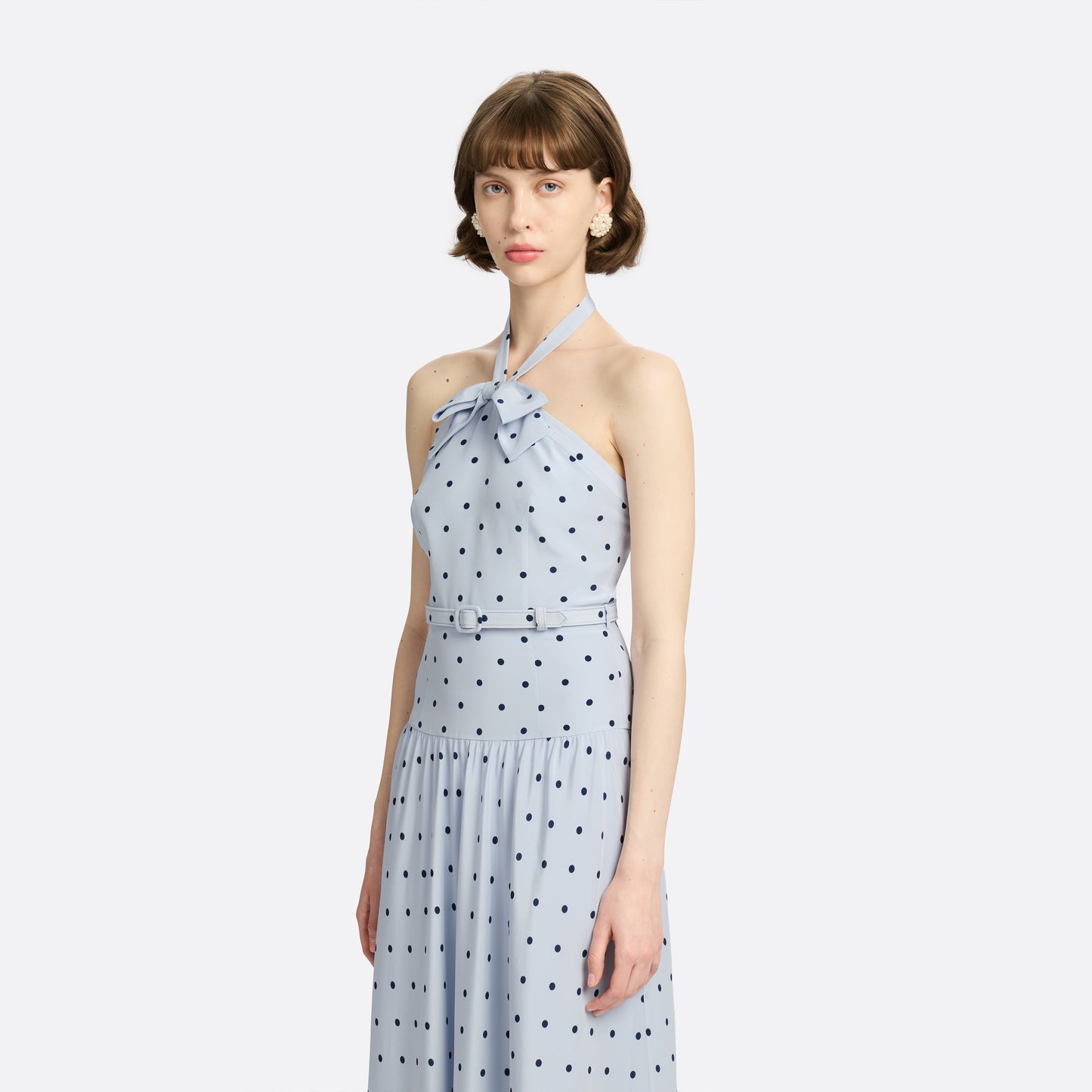 Light blue polka-dot silk crêpe de chine halterneck dress with a bow detail at the neckline. Defined by a fitted waist with a slim belt, the silhouette is finished with a flared skirt.