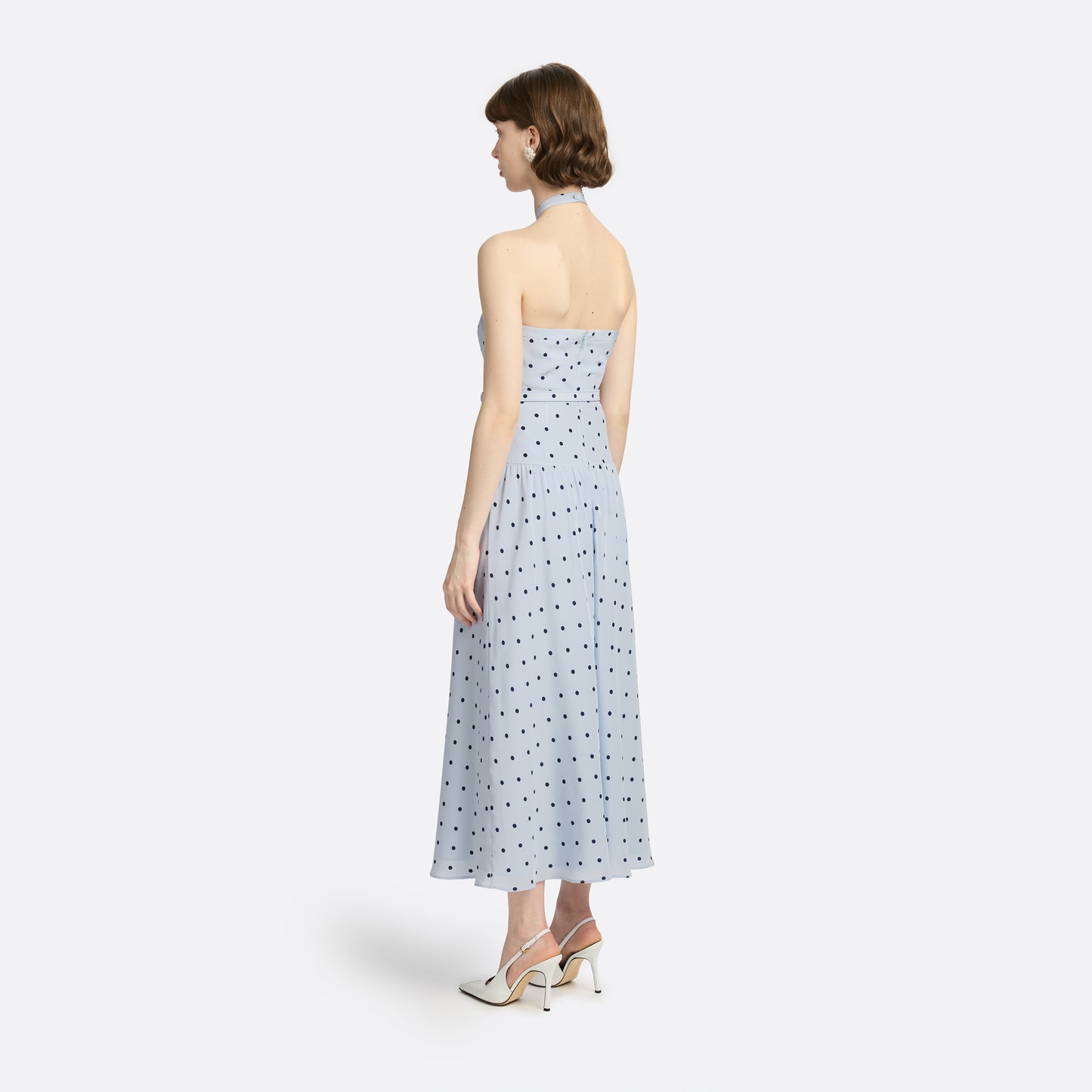 Light blue polka-dot silk crêpe de chine halterneck dress with a bow detail at the neckline. Defined by a fitted waist with a slim belt, the silhouette is finished with a flared skirt.