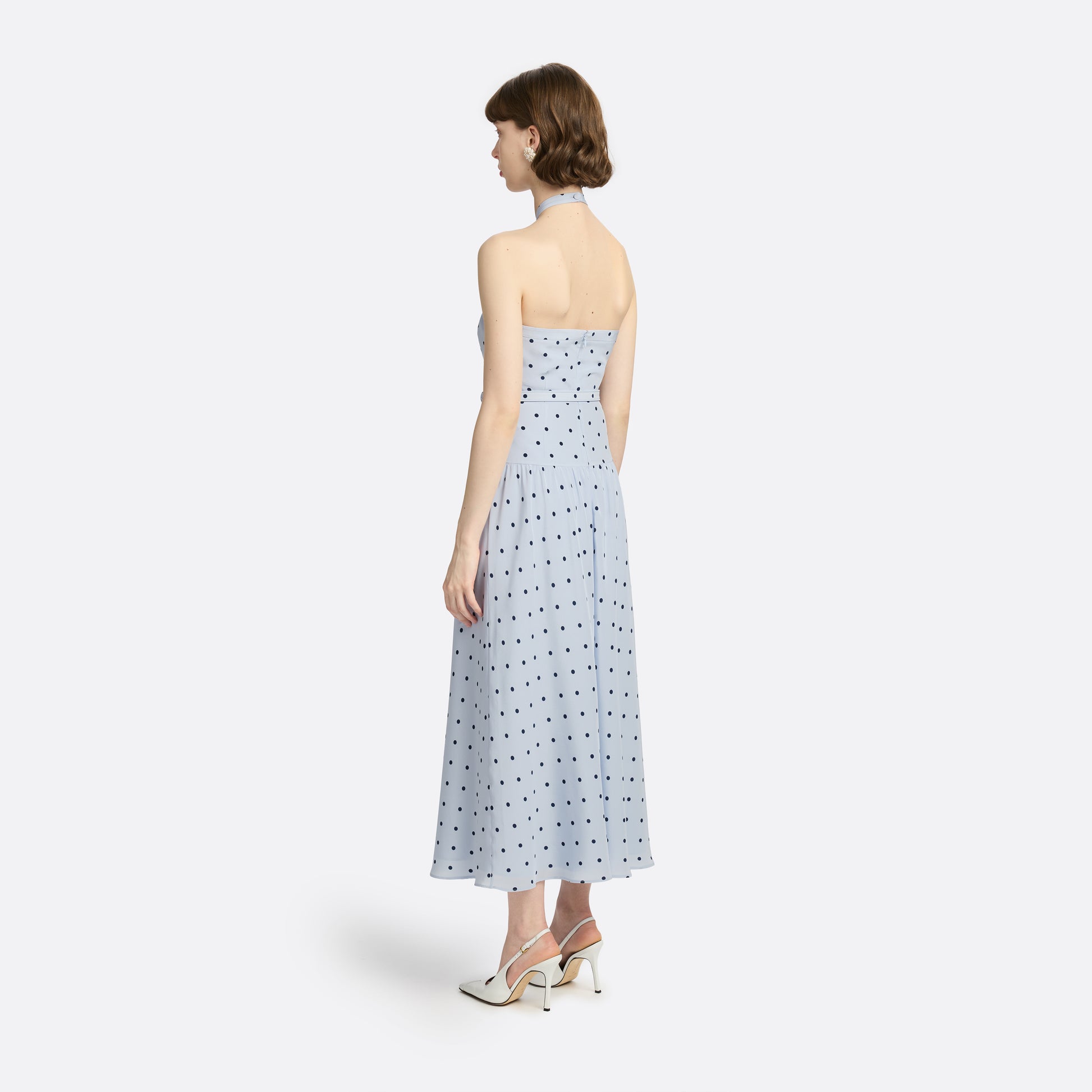 Light blue polka-dot silk crêpe de chine halterneck dress with a bow detail at the neckline. Defined by a fitted waist with a slim belt, the silhouette is finished with a flared skirt.