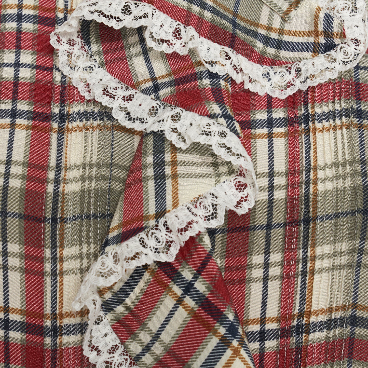 Red and green tartan-print  silk crêpe de chine blouse with small collar, jabot and short sleeves all trimmed in white lace. The blouse is fastened with a back button closure.

Look 32 – Fall Winter 2026 Lookbook.