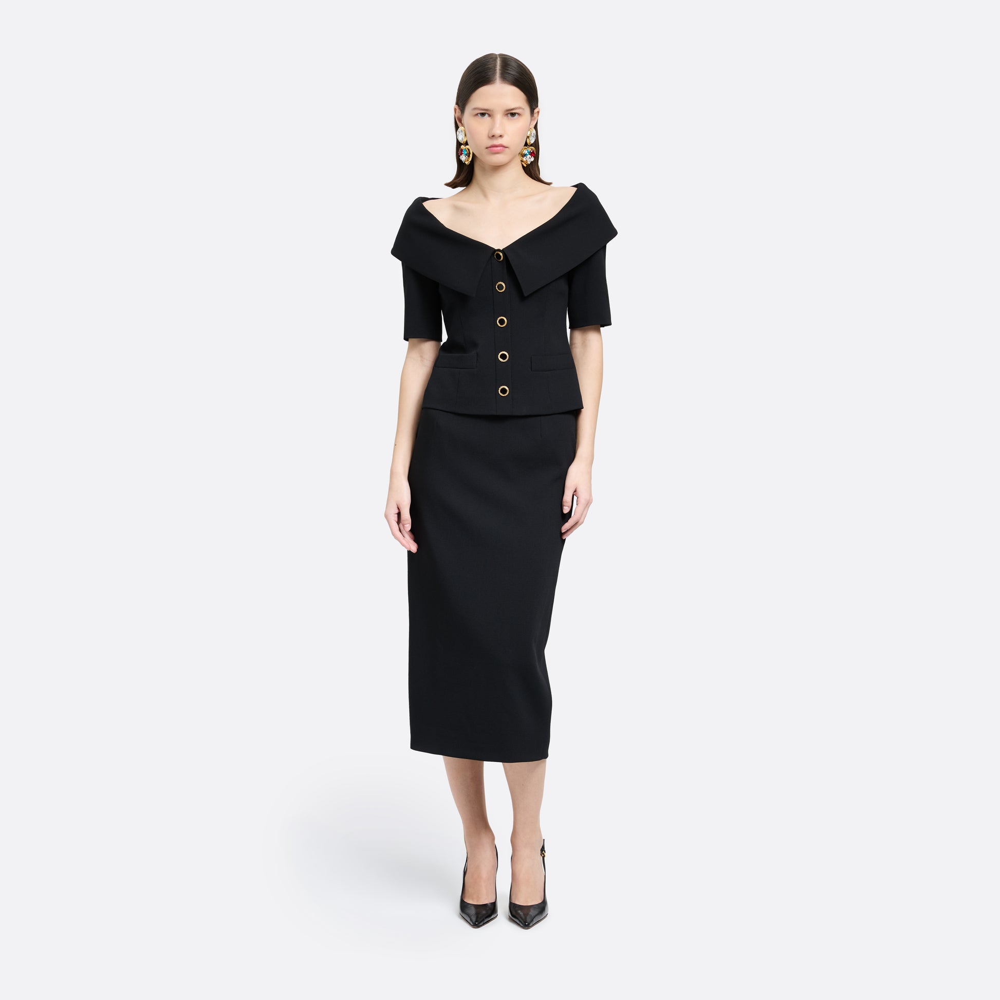 Black wool crêpe off-shoulder jacket with a wide folded neckline and short sleeves. Finished with black and gold-tone buttons and welt pockets.