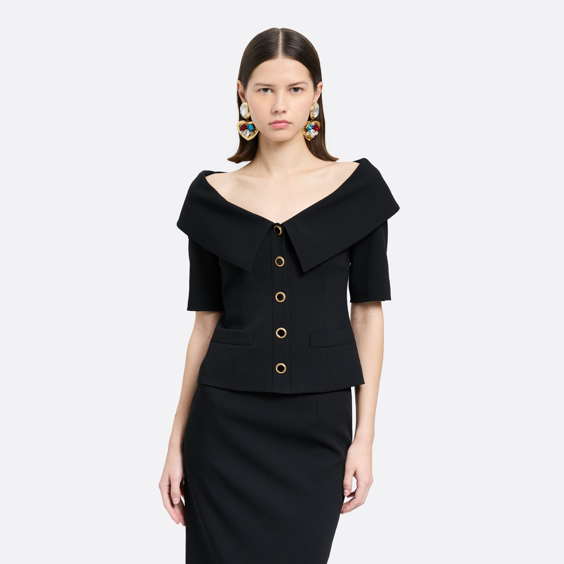 Black wool crêpe off-shoulder jacket with a wide folded neckline and short sleeves. Finished with black and gold-tone buttons and welt pockets.
