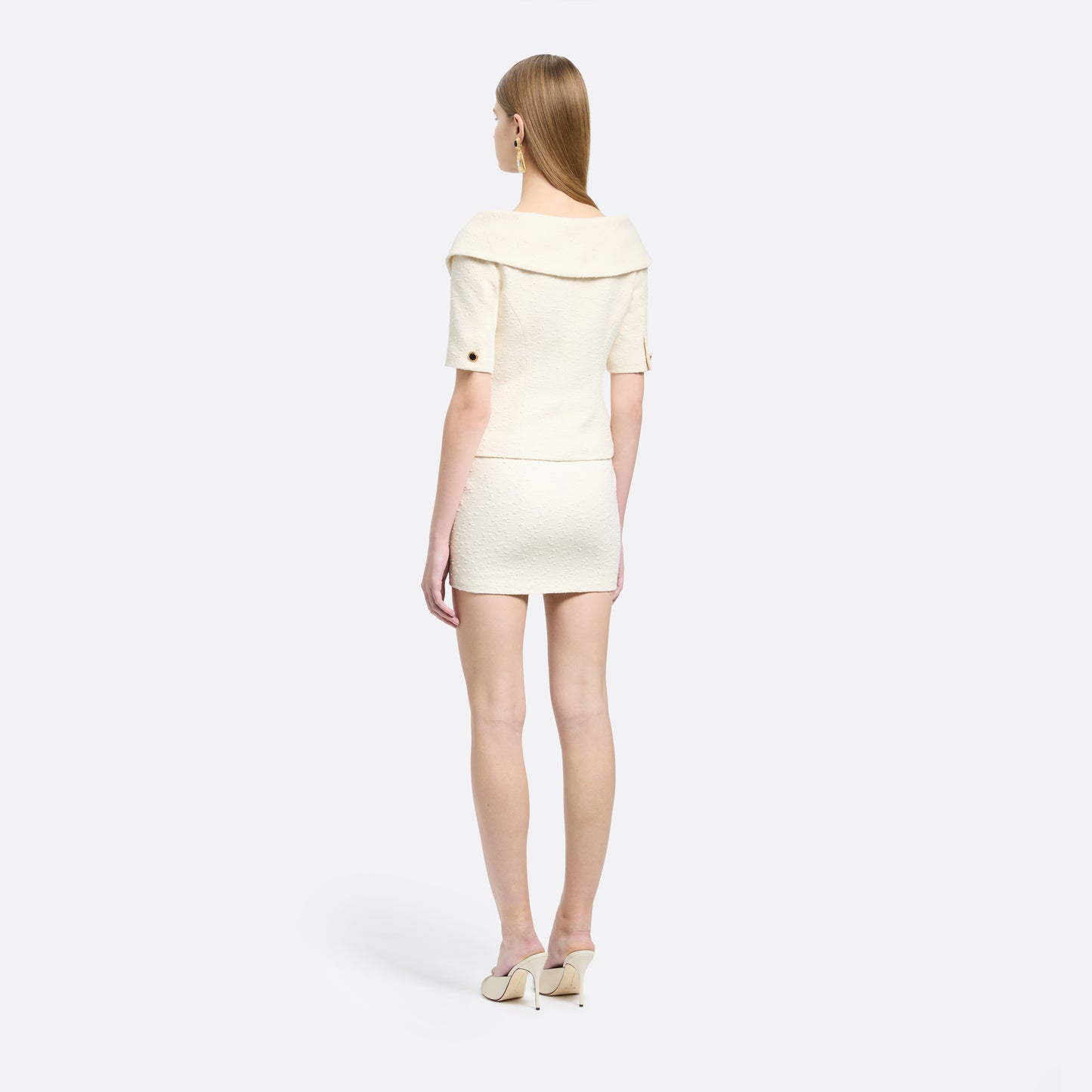 Ivory tweed bouclé off-shoulder jacket with a wide folded neckline and short sleeves. Finished with black and gold-tone buttons and welt pockets.