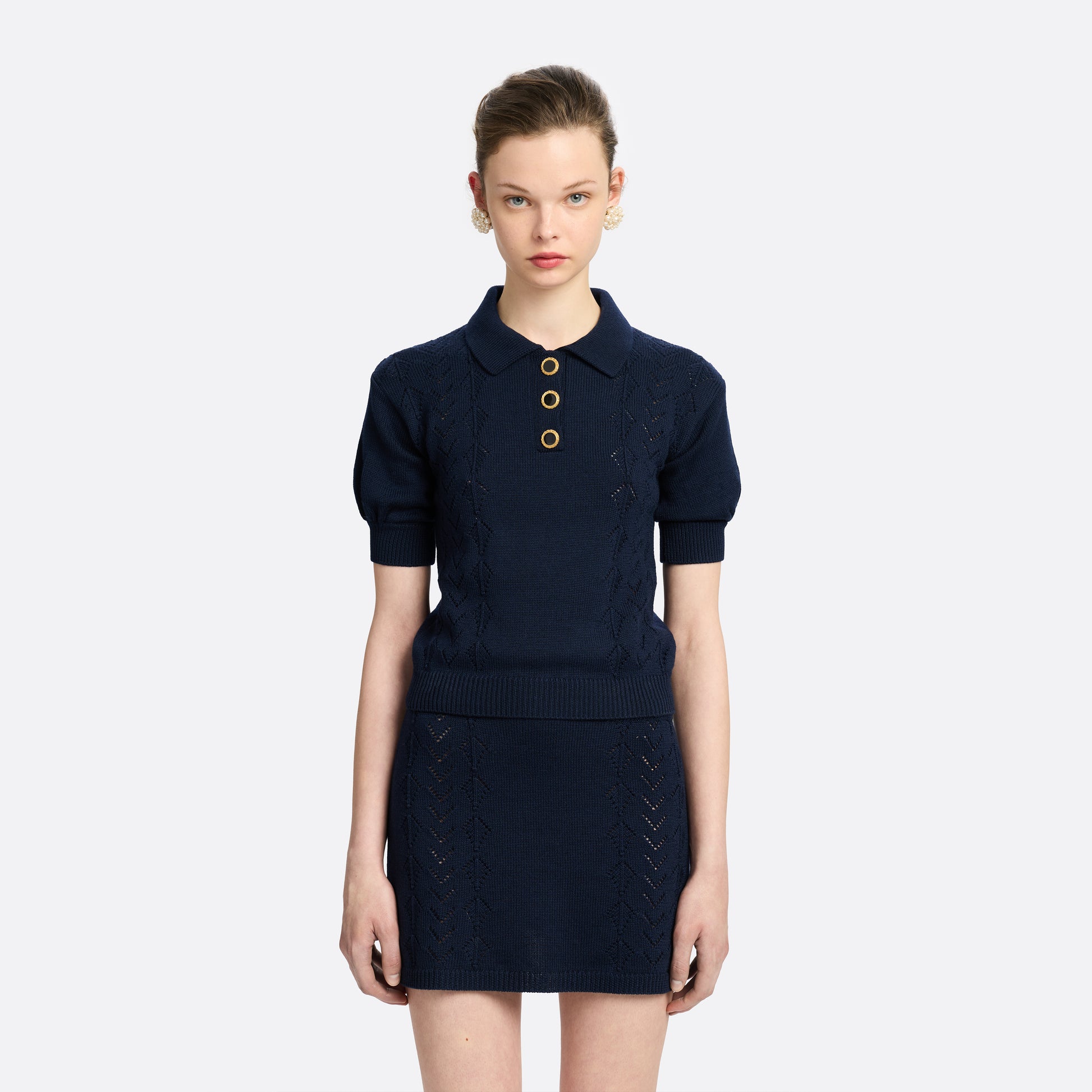 Navy blue merino wool lace-knit polo cut to a fitted silhouette with short puff sleeves and black and gold-tone buttons.