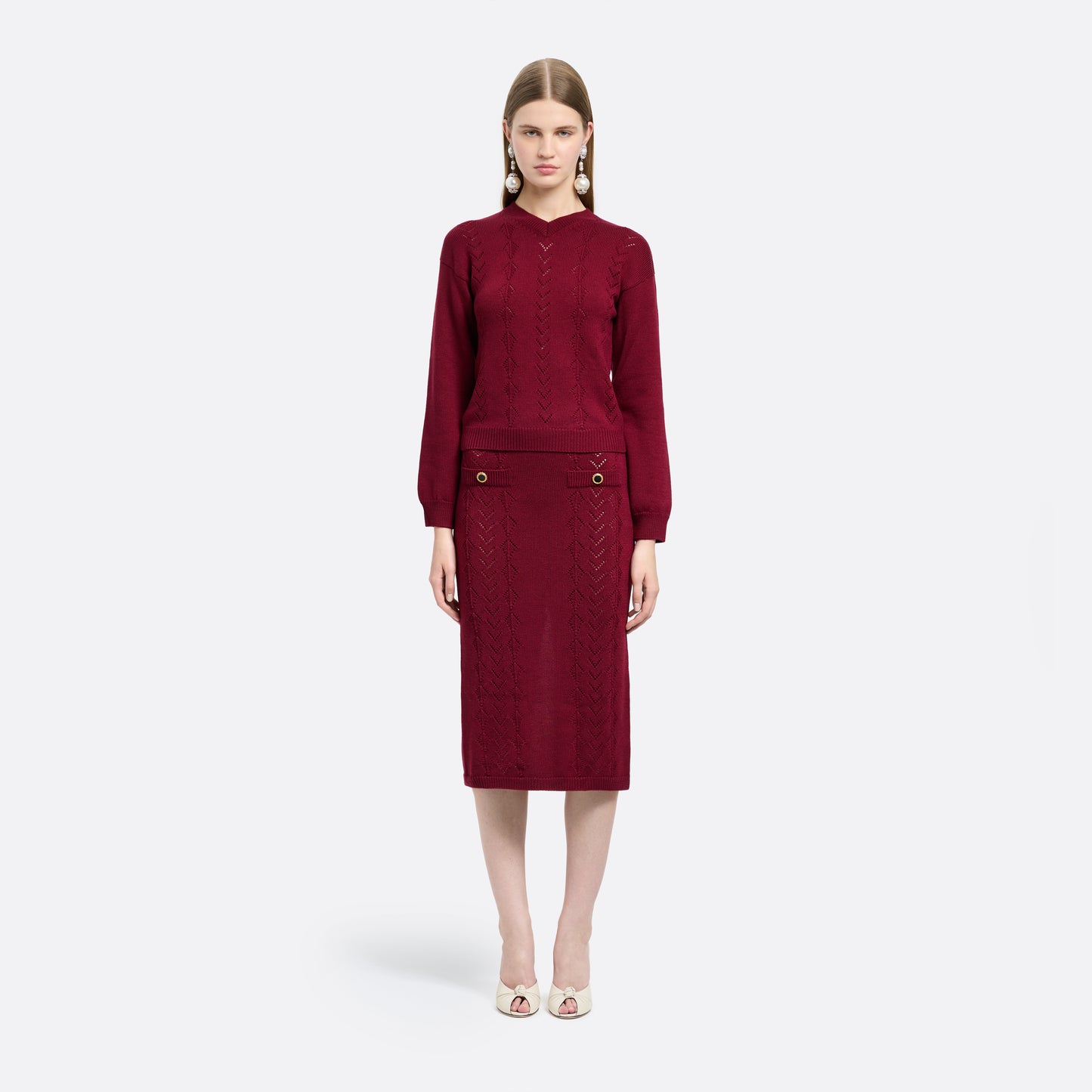 Bordeaux merino wool lace-knit midi skirt cut in a fitted silhouette. Finished with decorative pockets and black and gold-tone buttons.