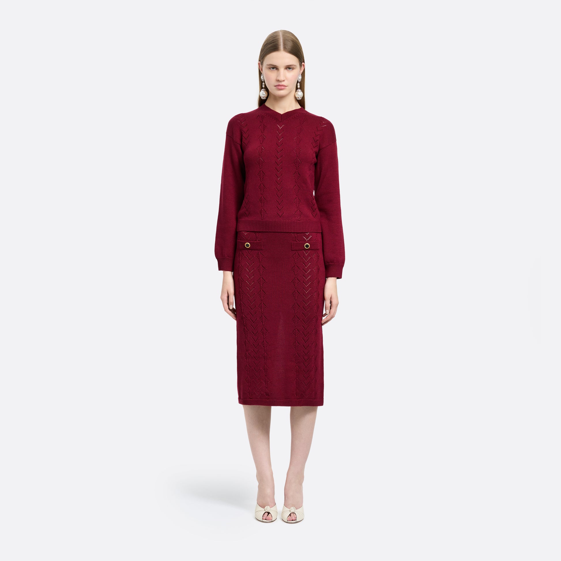 Bordeaux merino wool lace-knit midi skirt cut in a fitted silhouette. Finished with decorative pockets and black and gold-tone buttons.