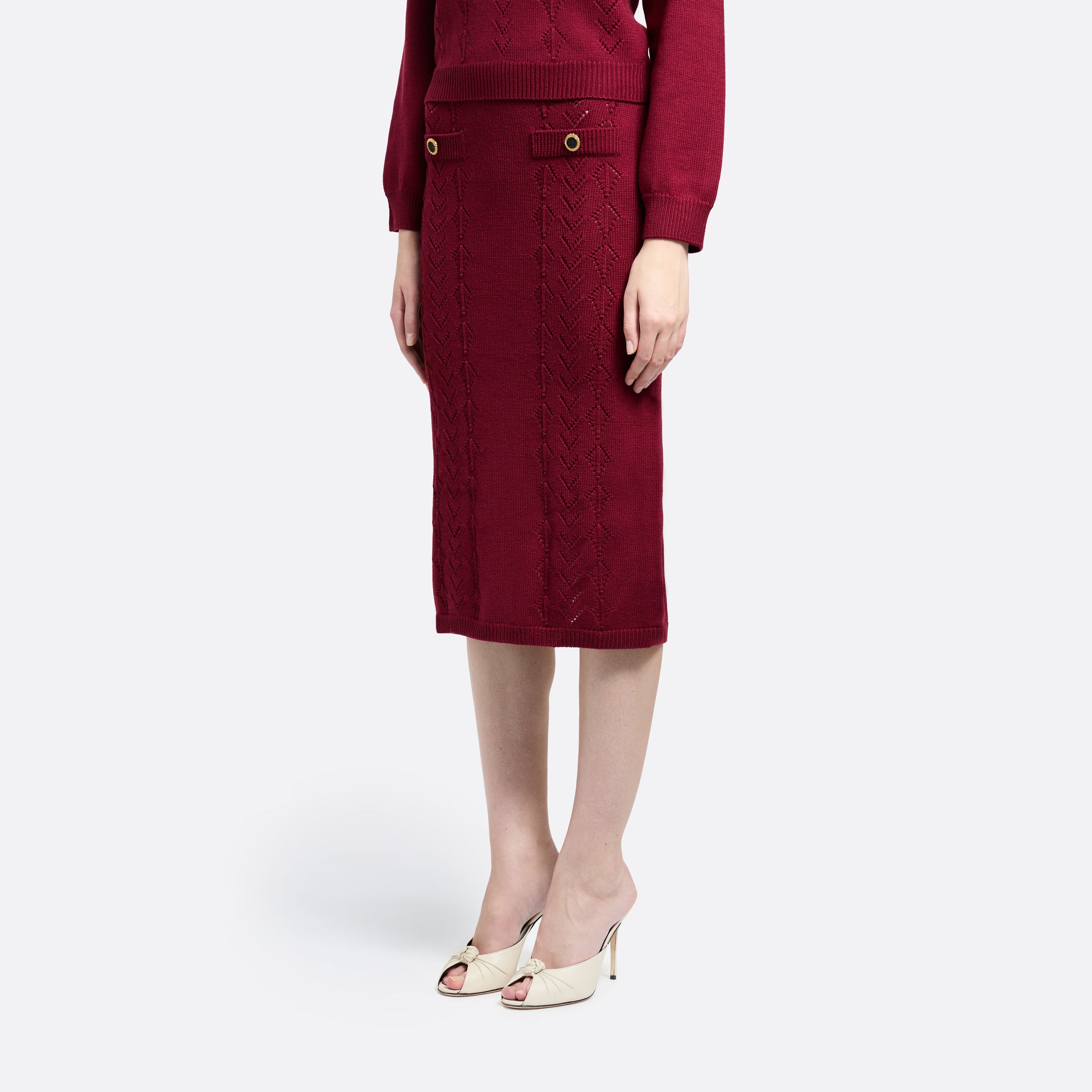 Bordeaux merino wool lace-knit midi skirt cut in a fitted silhouette. Finished with decorative pockets and black and gold-tone buttons.