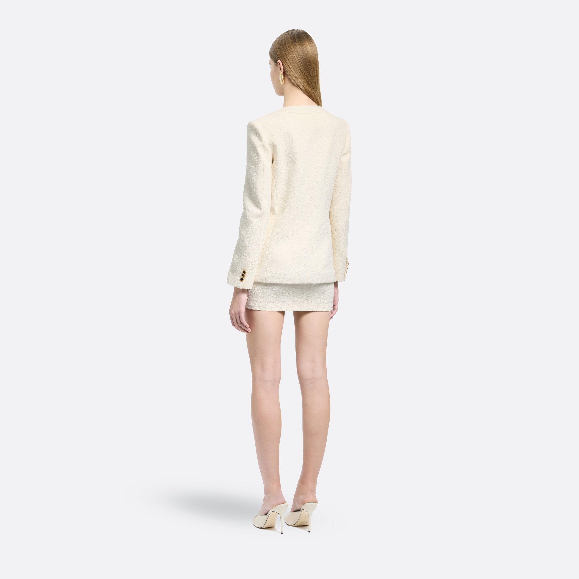 Ivory tweed bouclé jacket cut to a longline silhouette with a V-neckline and patch pockets. Finished with black and gold-tone buttons and a bow detail.