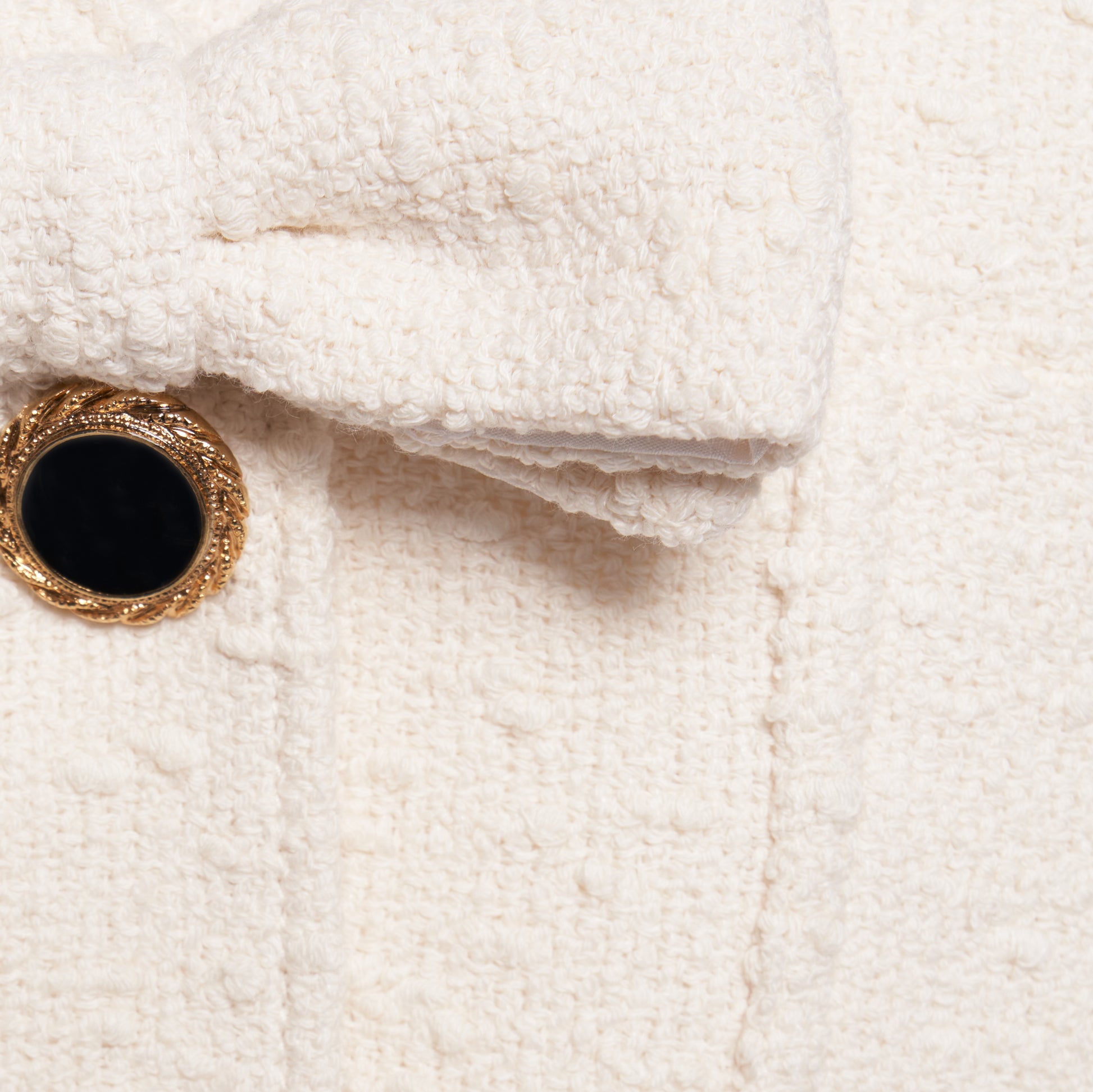 Ivory tweed bouclé jacket cut to a longline silhouette with a V-neckline and patch pockets. Finished with black and gold-tone buttons and a bow detail.
