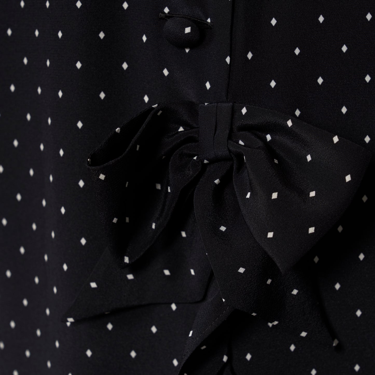 Ivory diamond print on black silk crêpe de chine sleeveless midi dress with a high ruffled neckline, featuring button detail, side split and bow.
