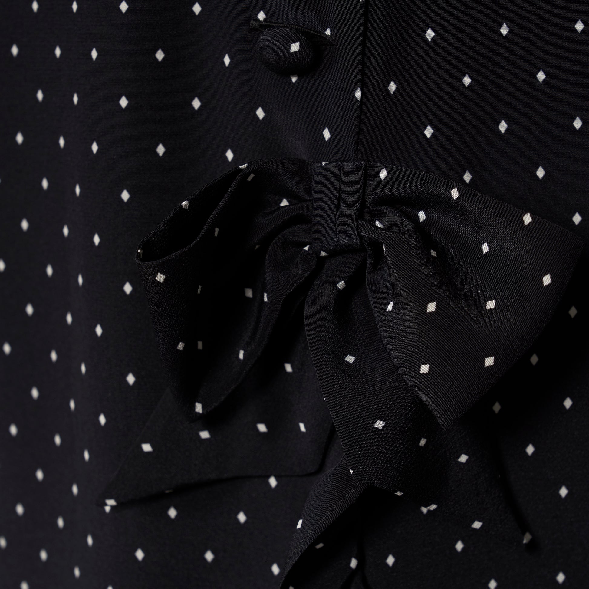 Ivory diamond print on black silk crêpe de chine sleeveless midi dress with a high ruffled neckline, featuring button detail, side split and bow.