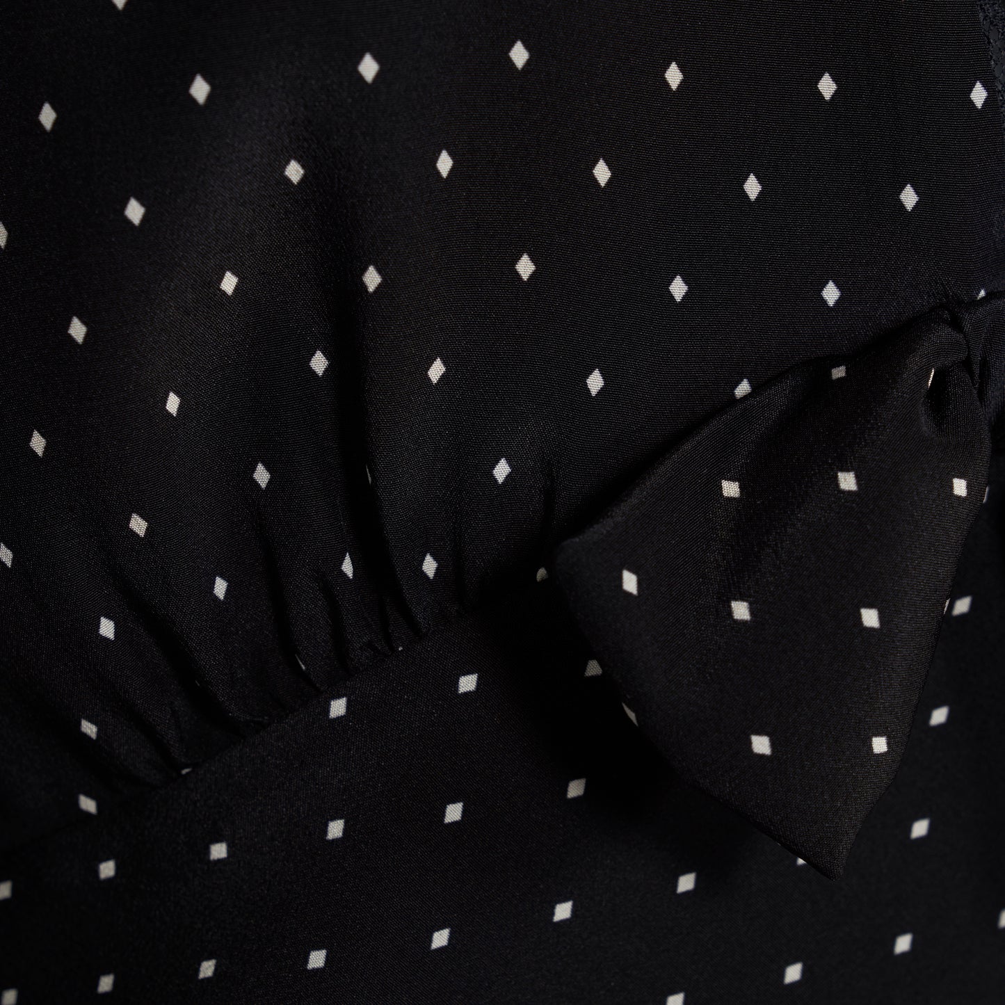 Ivory diamond print on black silk crêpe de chine mini dress with a V neckline and short sleeves, featuring lace trims and a bow.
