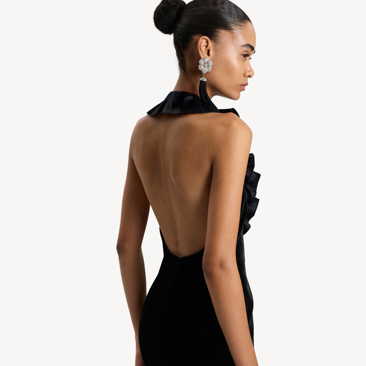 Black velvet evening dress featuring an open back and a deep neckline with a silk ruffle trim.