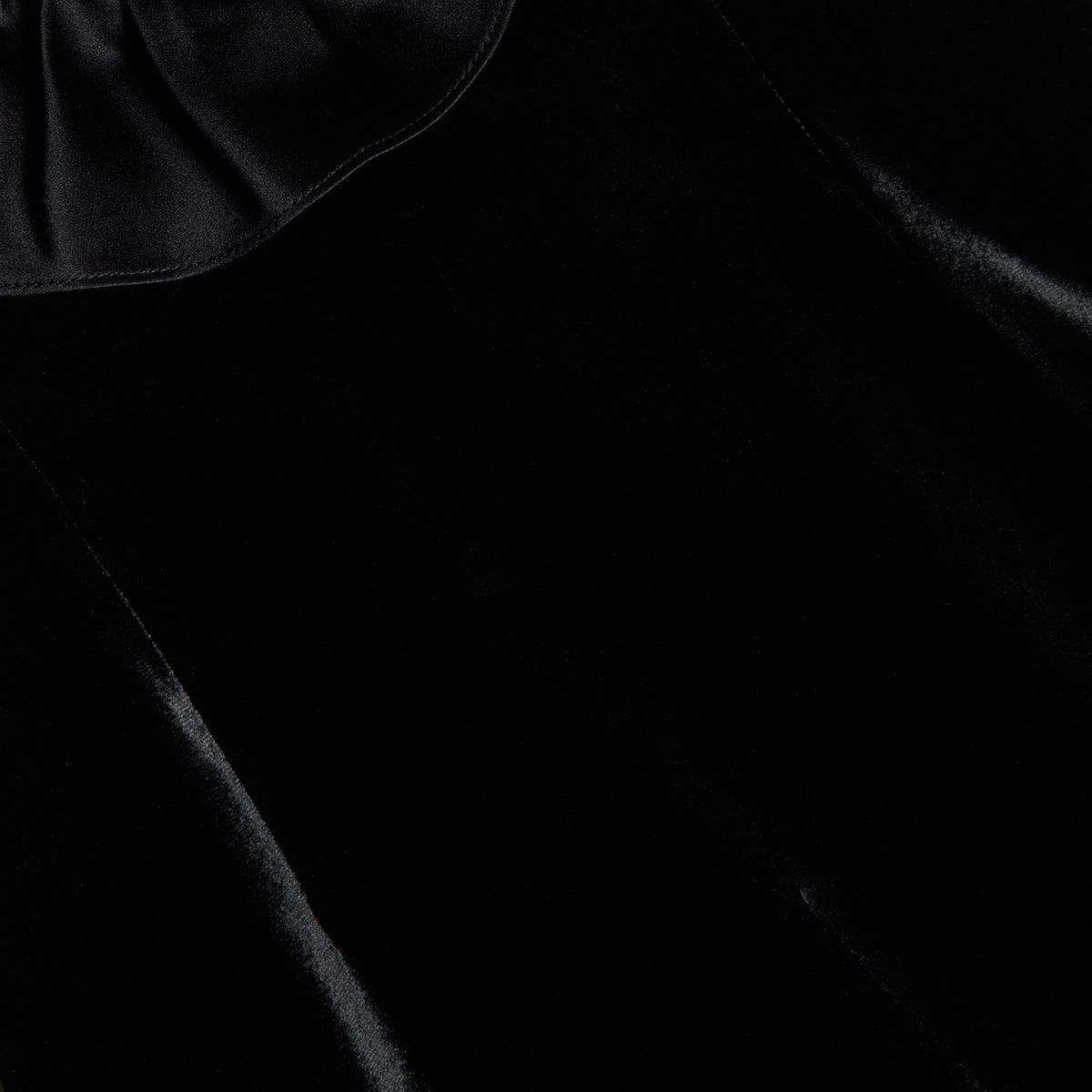 Black velvet evening dress featuring an open back and a deep neckline with a silk ruffle trim.